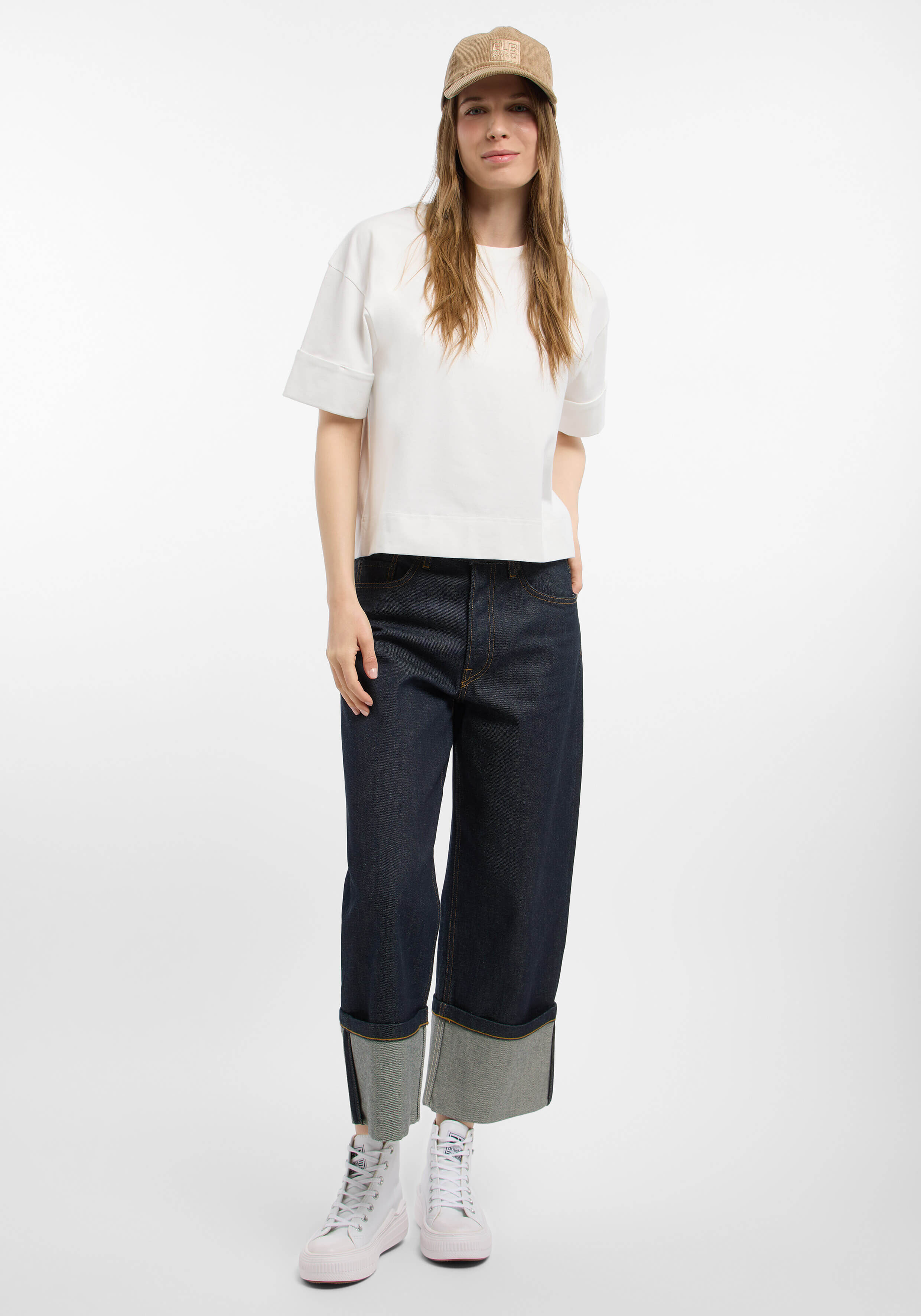 Frau in weißem T-Shirt, dunklen Jeans mit weitem Bein und beiger Mütze für lässigen Stil.