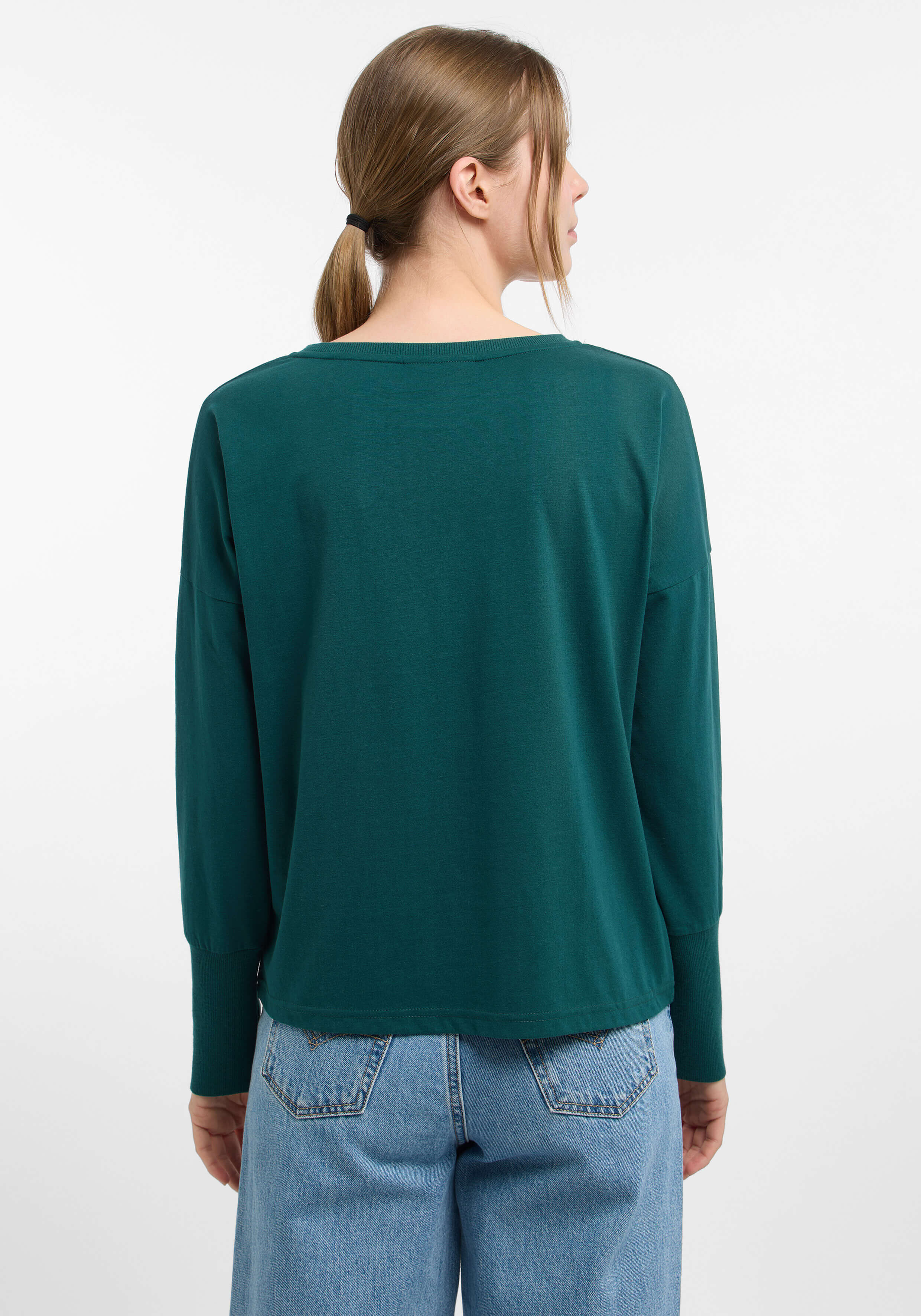 Rückansicht einer Frau in einem grünen Langarmshirt und blauen Jeans.