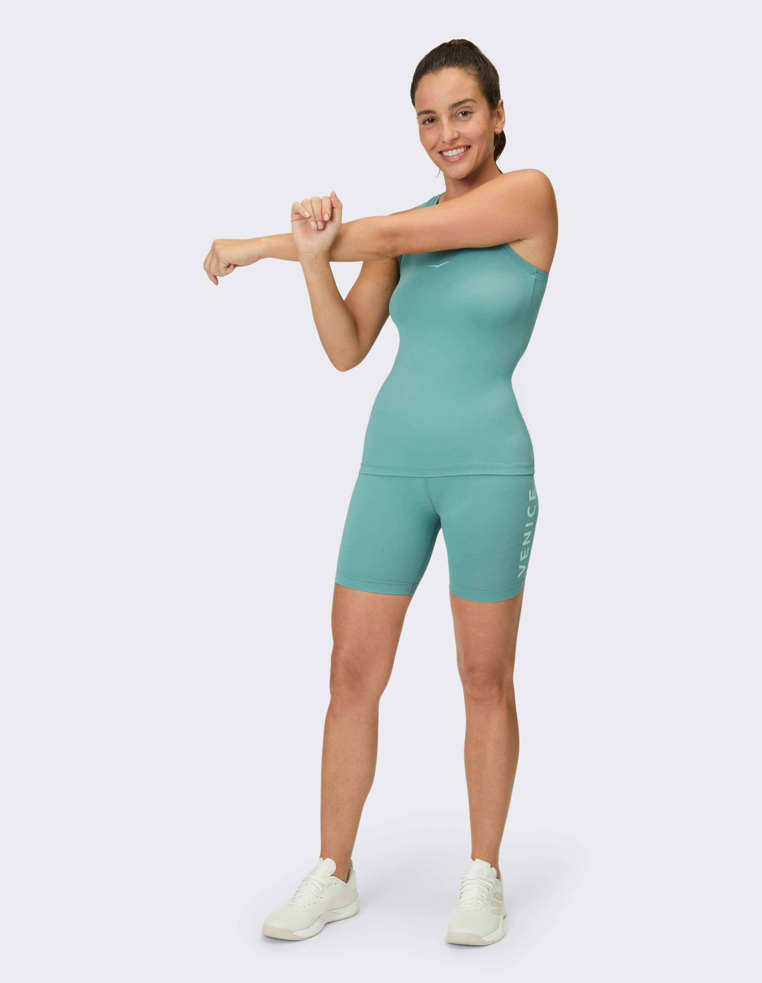 Frau trägt ein blaugrünes Tanktop und passende Radlershorts für einen sportlichen, lässigen Look.