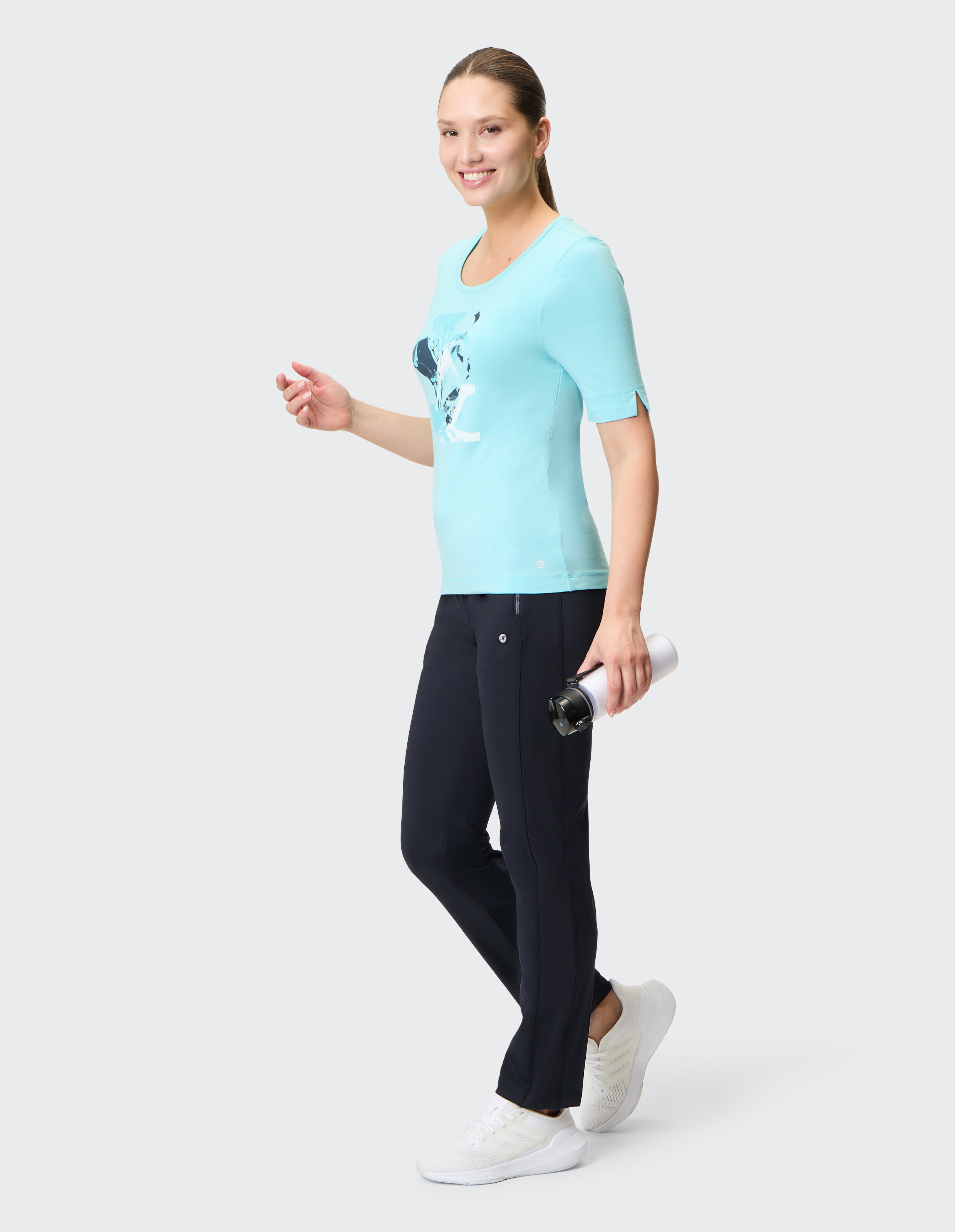 Frau trägt ein hellblaues Grafik-T-Shirt und eine dunkle Hose für einen lässigen, aktiven Look.