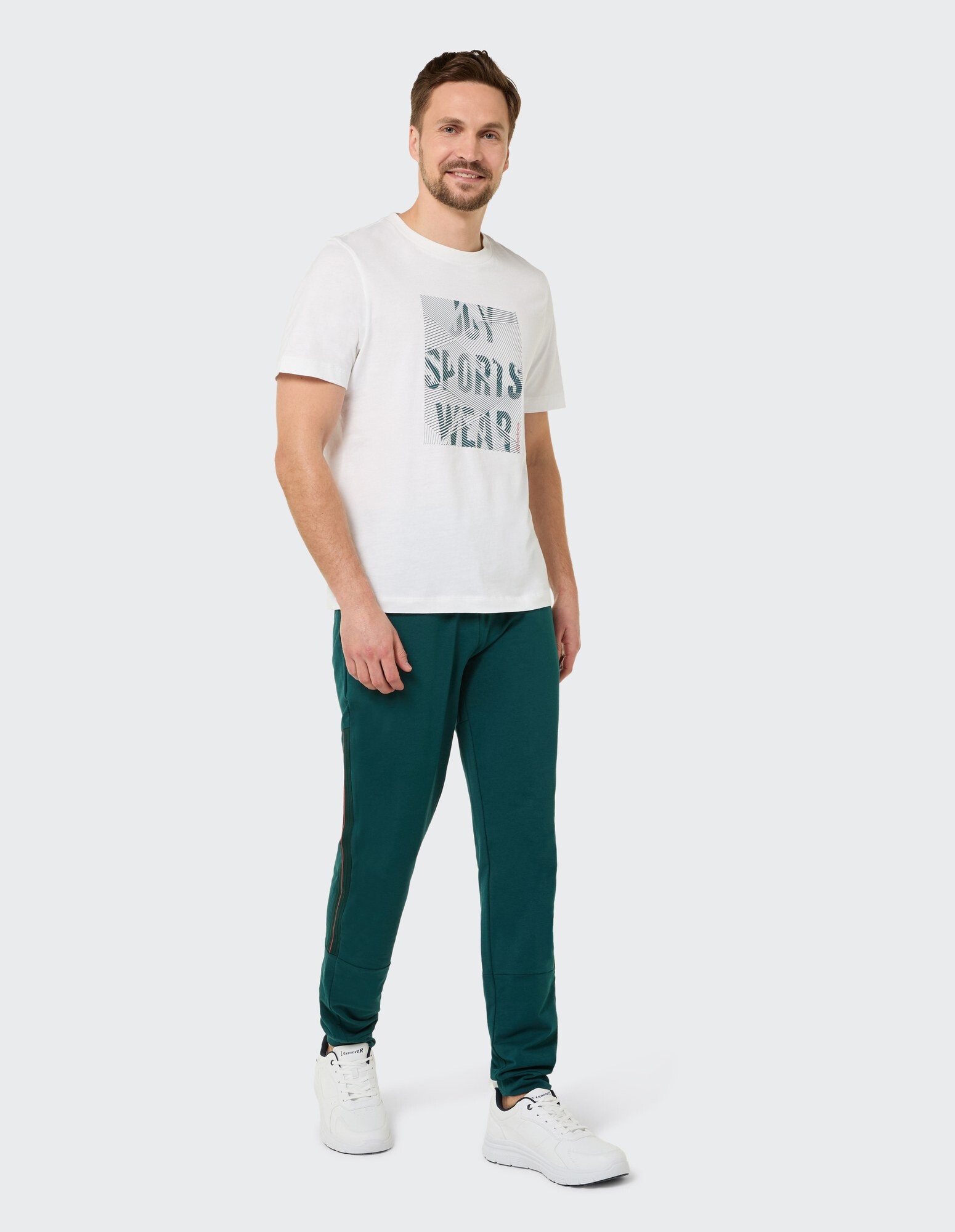 Mann in einem weißen Grafik-T-Shirt und grünen Jogginghosen, perfekt für Freizeitkleidung.