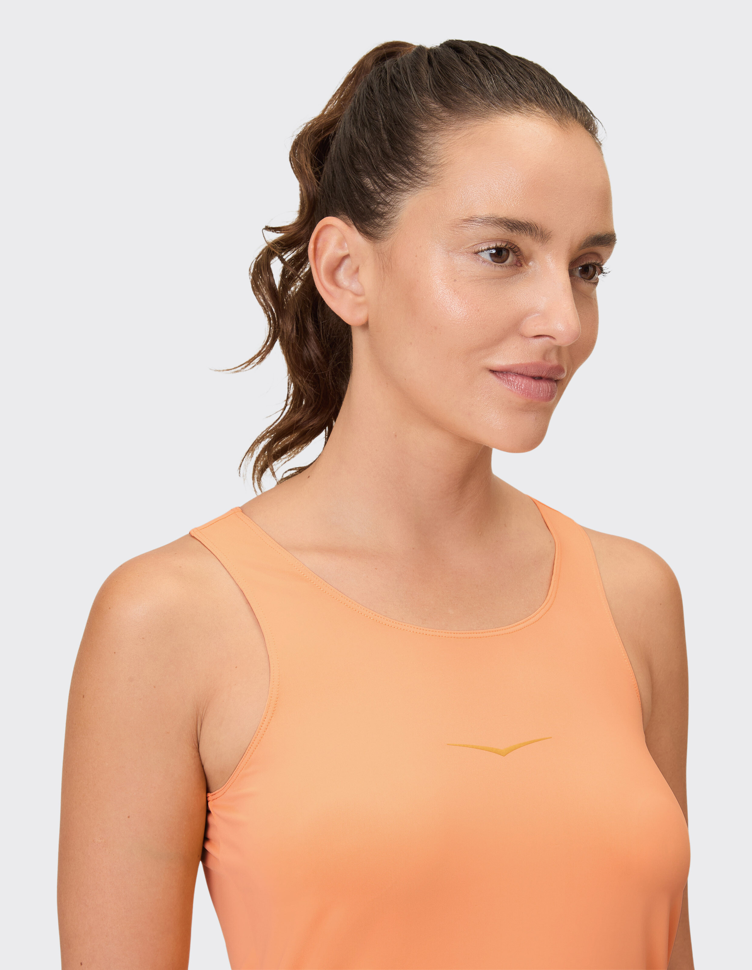 Nahaufnahme einer Frau, die ein pfirsichfarbenes Tanktop mit dezentem Logo trägt und einen lässigen Stil unterstreicht.