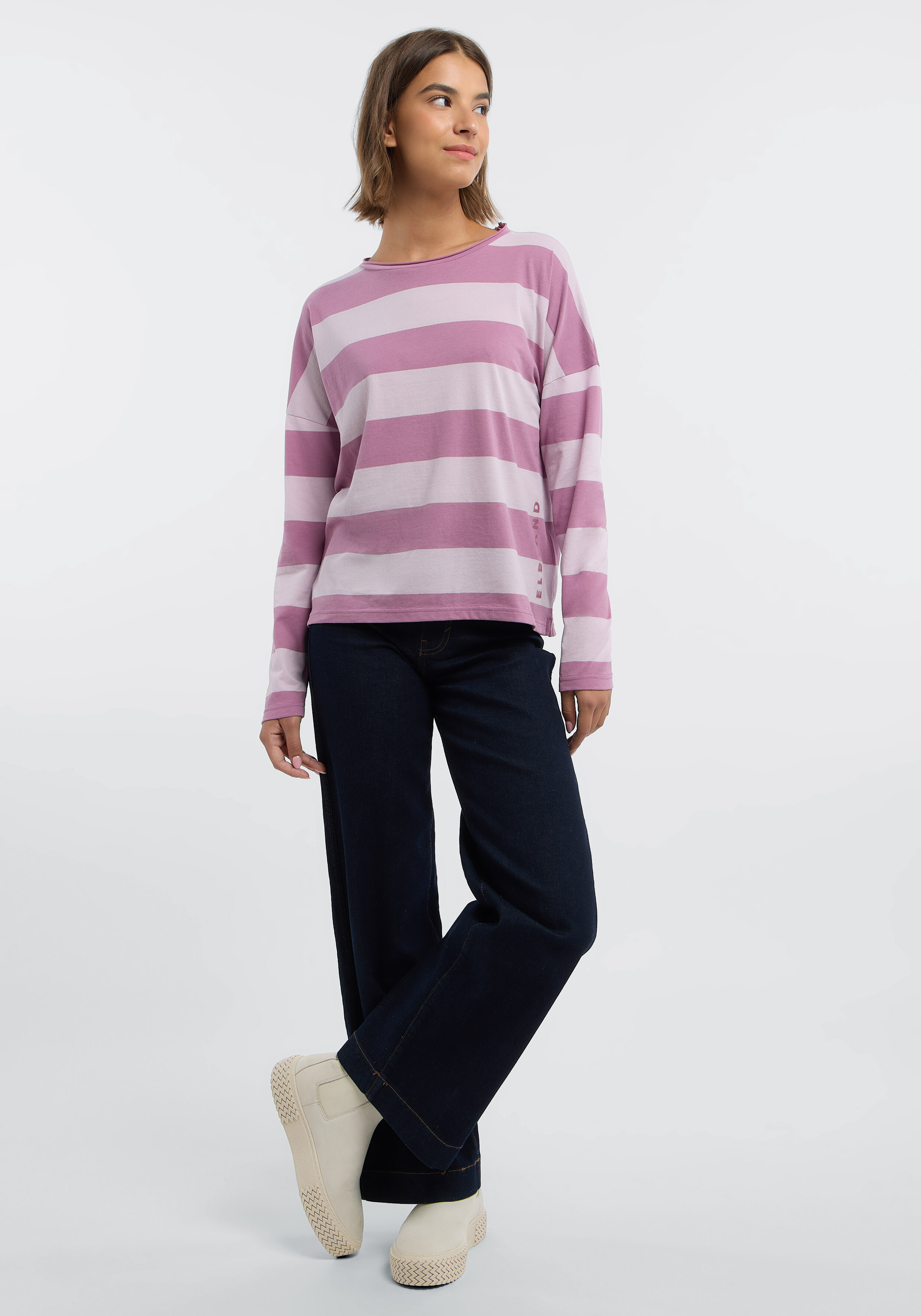 Frau trägt ein gemütliches rosa gestreiftes Langarmhemd und dunkle Jeans für einen lässigen Stil.