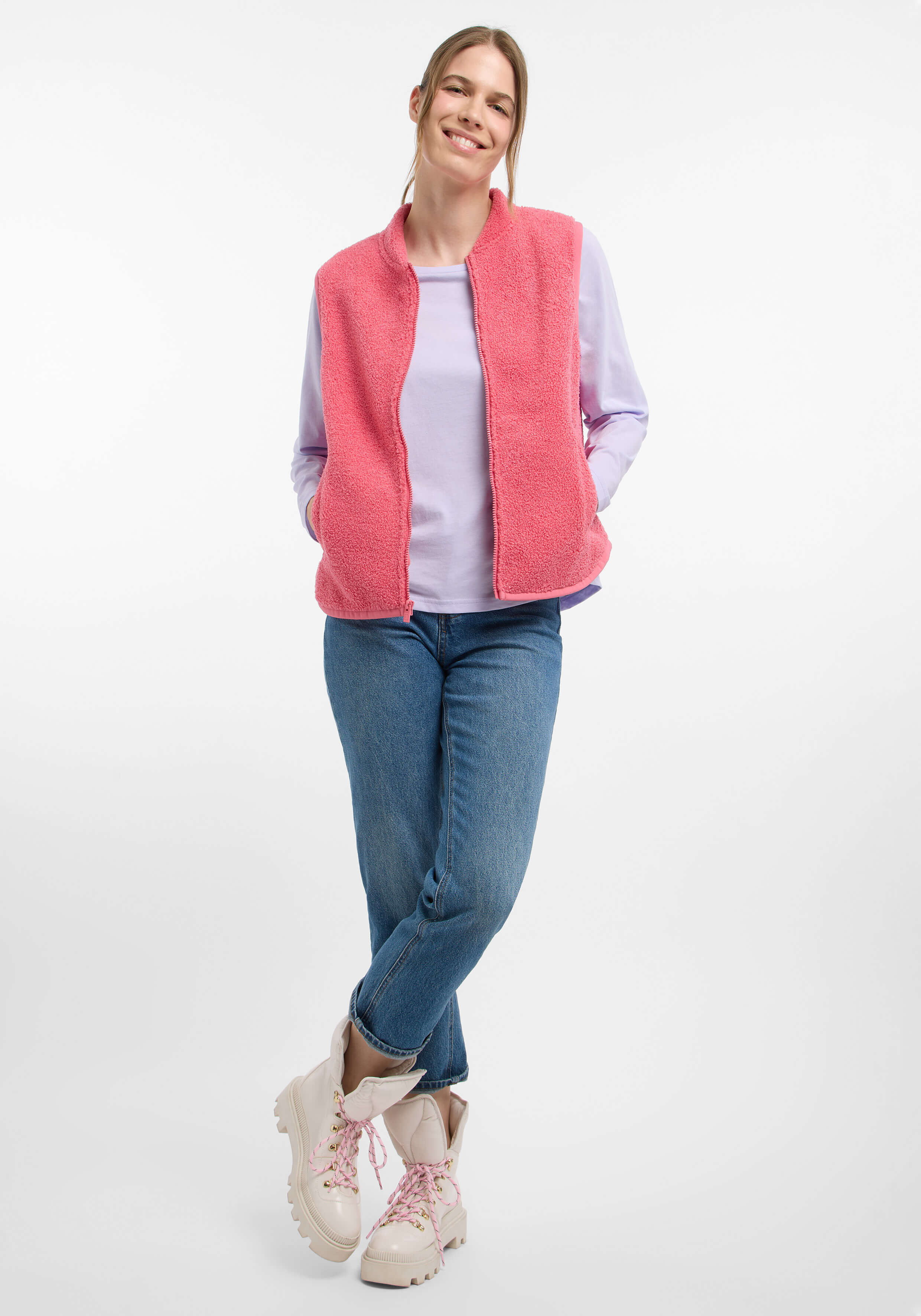 Frau trägt eine kuschelige rosa Fleeceweste, ein lila Langarmhemd und blaue Jeans.