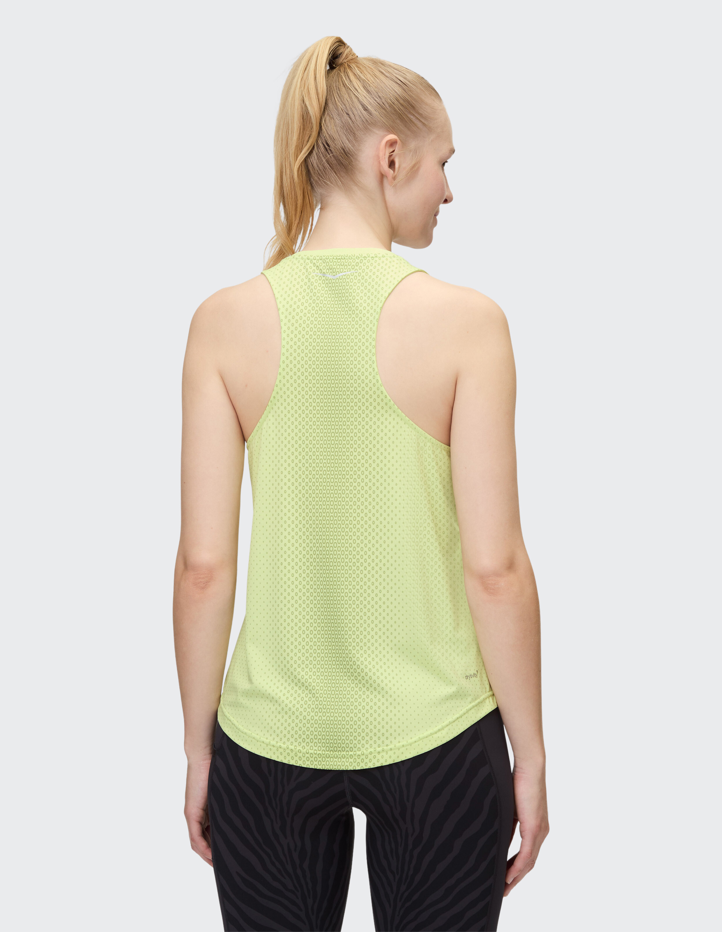 Rückansicht einer Frau in einem hellgrünen Netz-Tanktop und gemusterten Leggings.