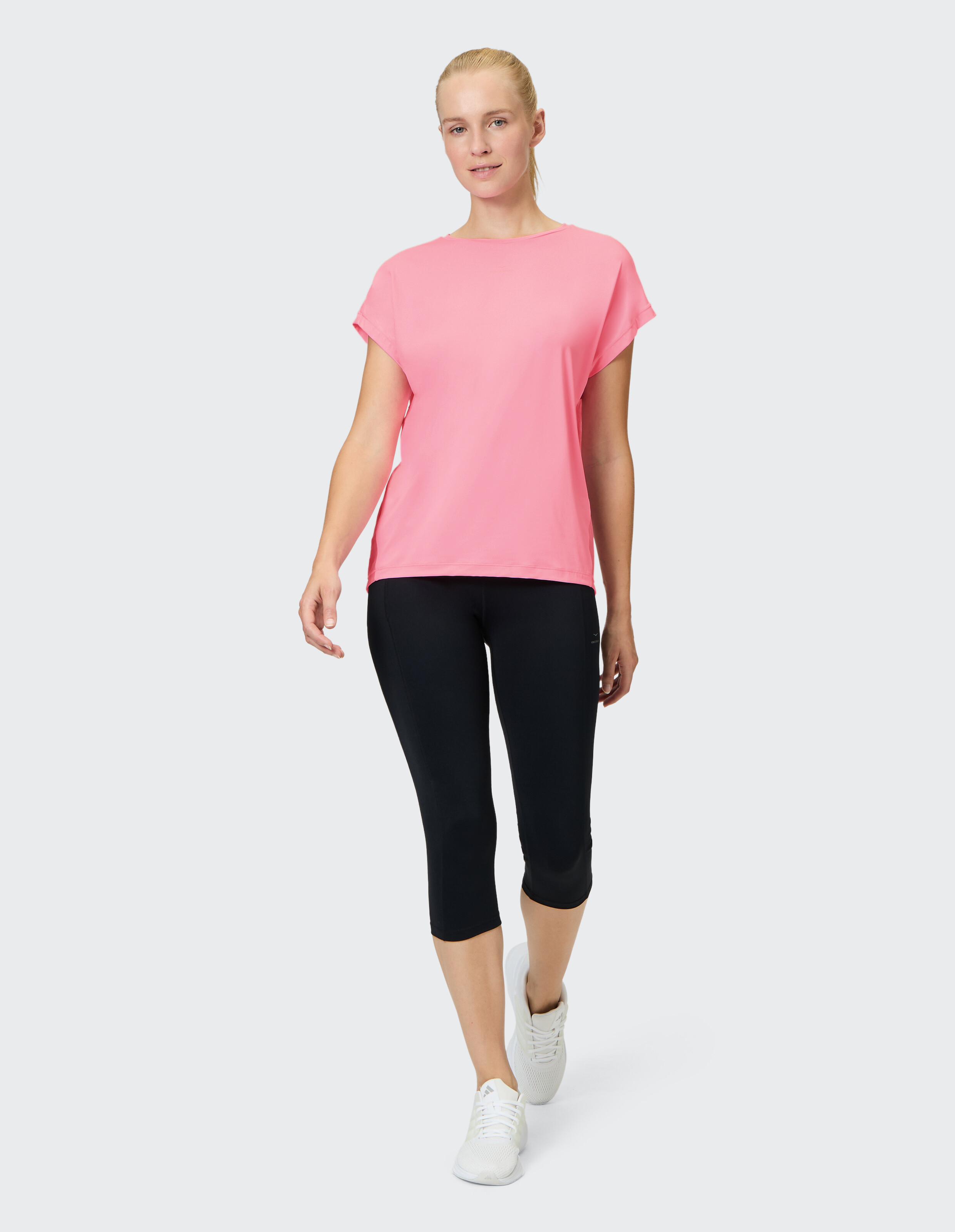 Frau trägt ein rosa Freizeit-T-Shirt und schwarze Capri-Leggings für Aktivkleidung.
