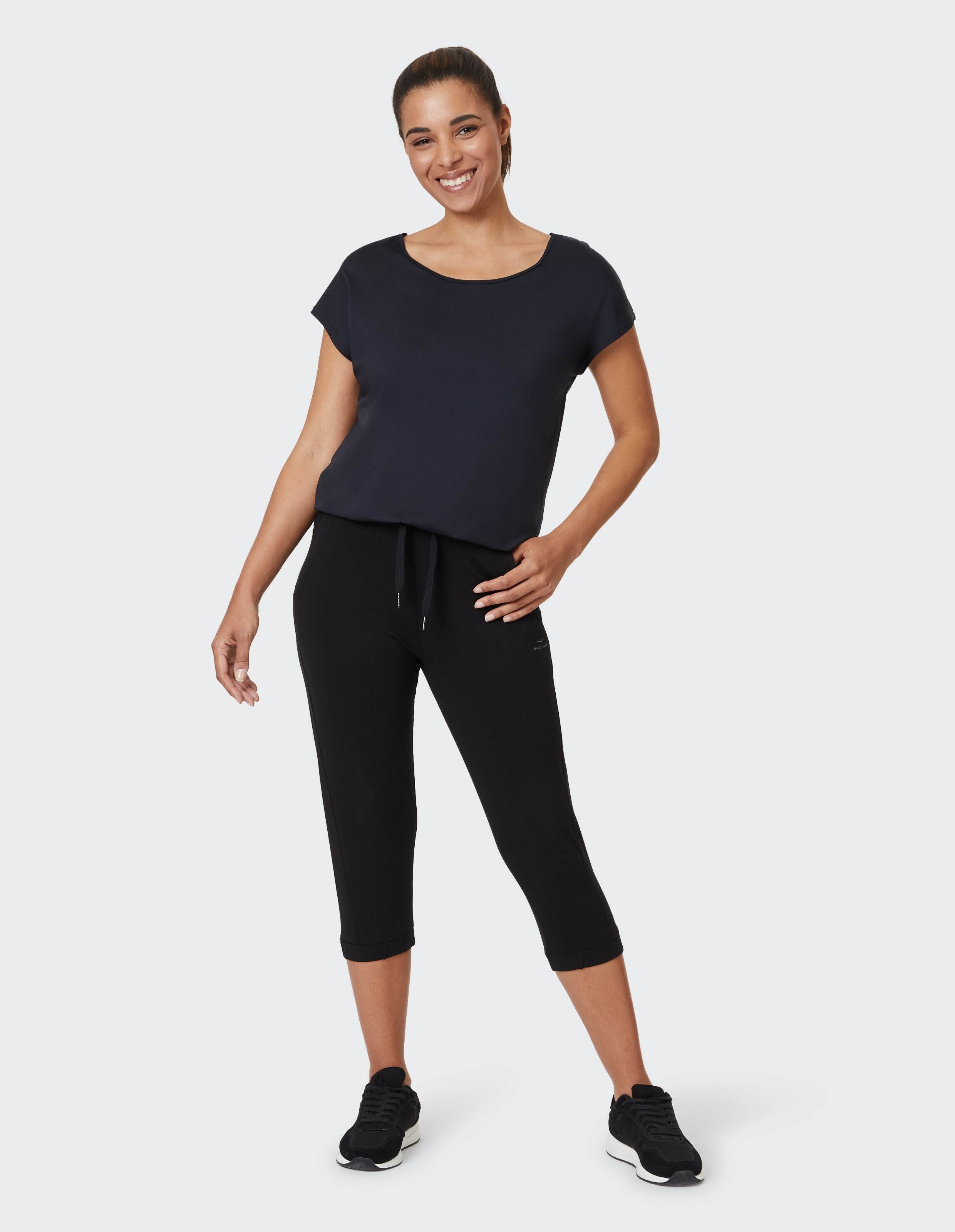 Frau in dunkelblauem Top und schwarzer Caprihose, lächelnd in Freizeitkleidung.