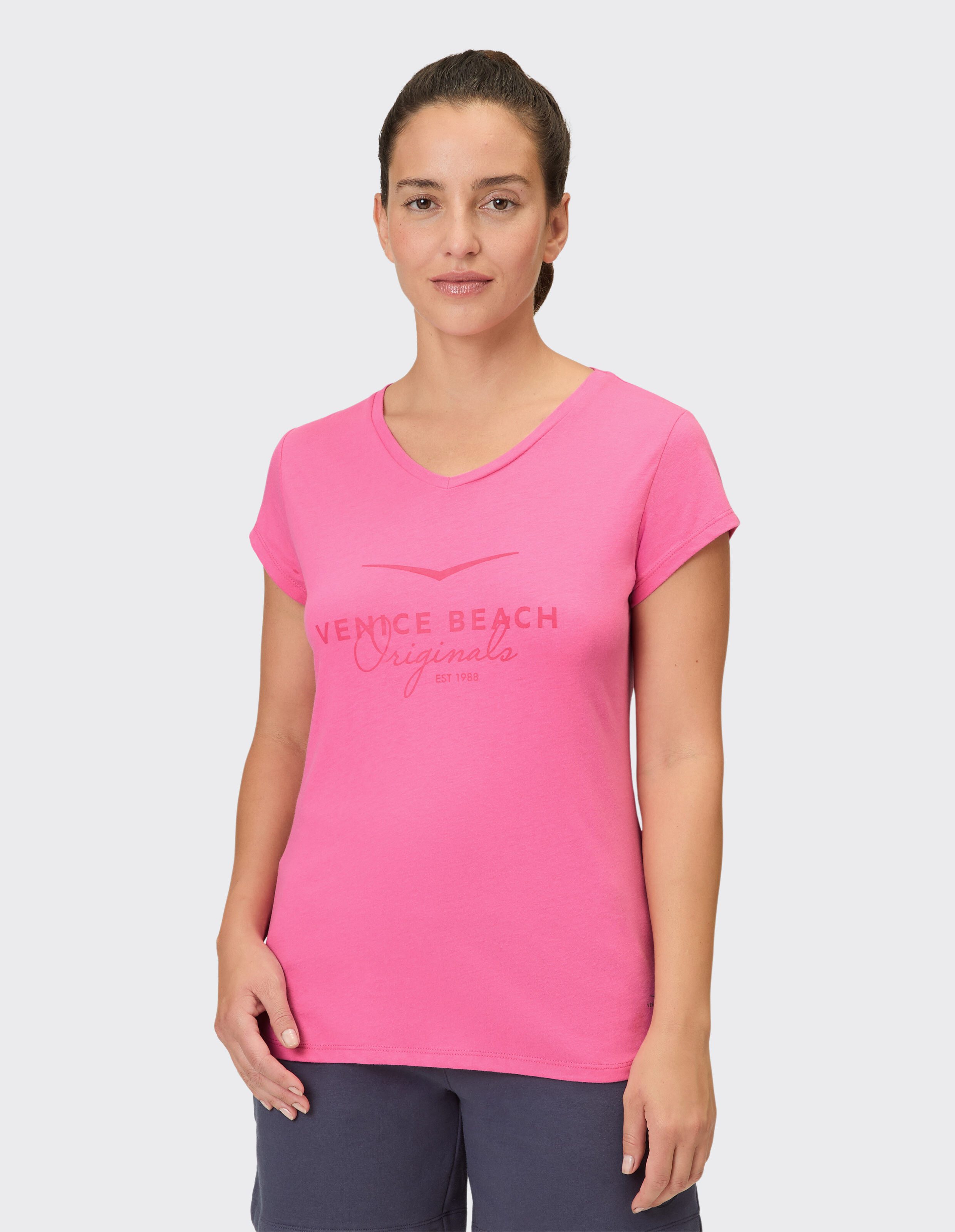 Frau trägt ein rosa lässiges T-Shirt mit V-Ausschnitt und Venice Beach-Logoaufdruck.