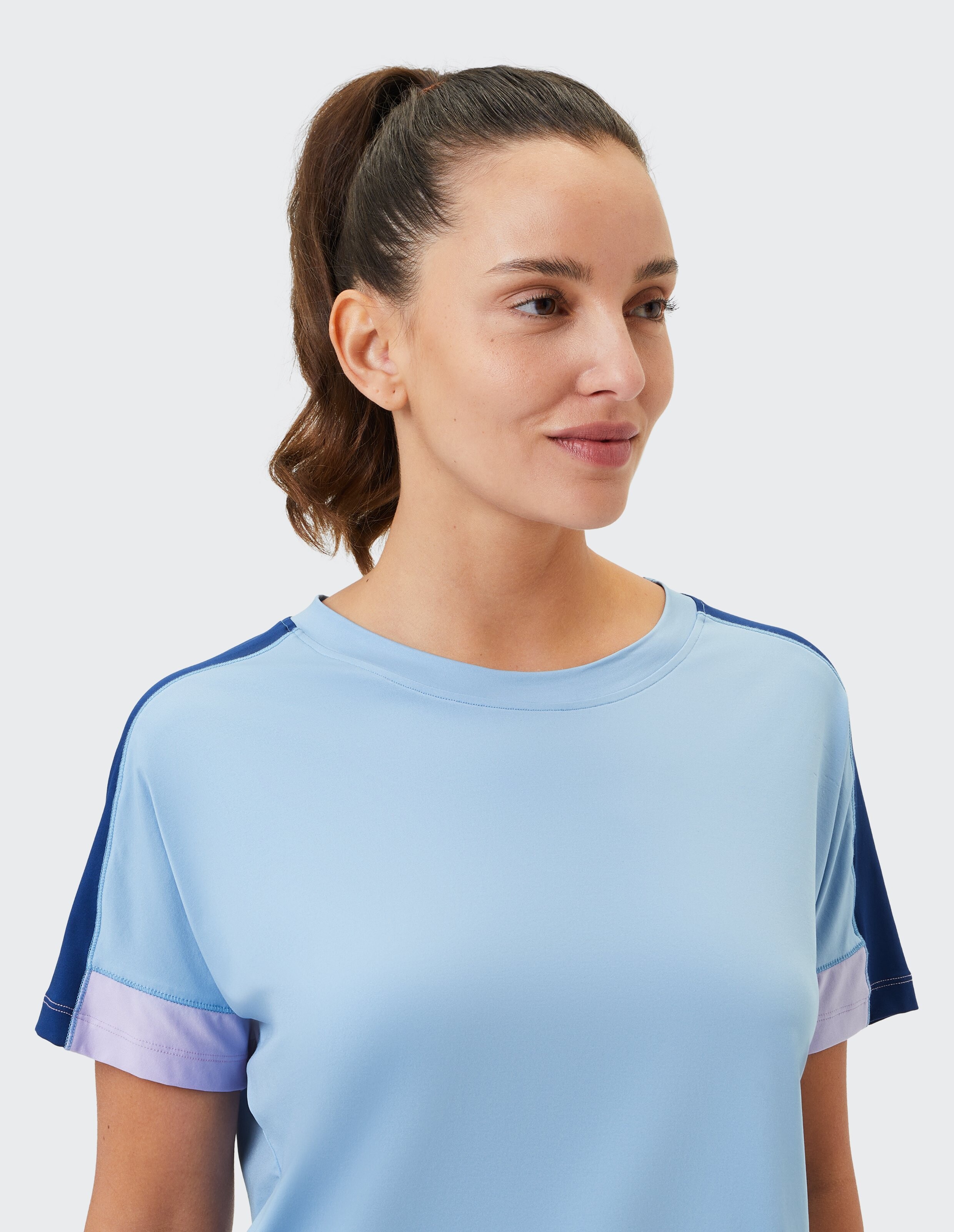 Nahaufnahme einer Frau in einem hellblauen Freizeit-T-Shirt mit bunten Ärmeln.