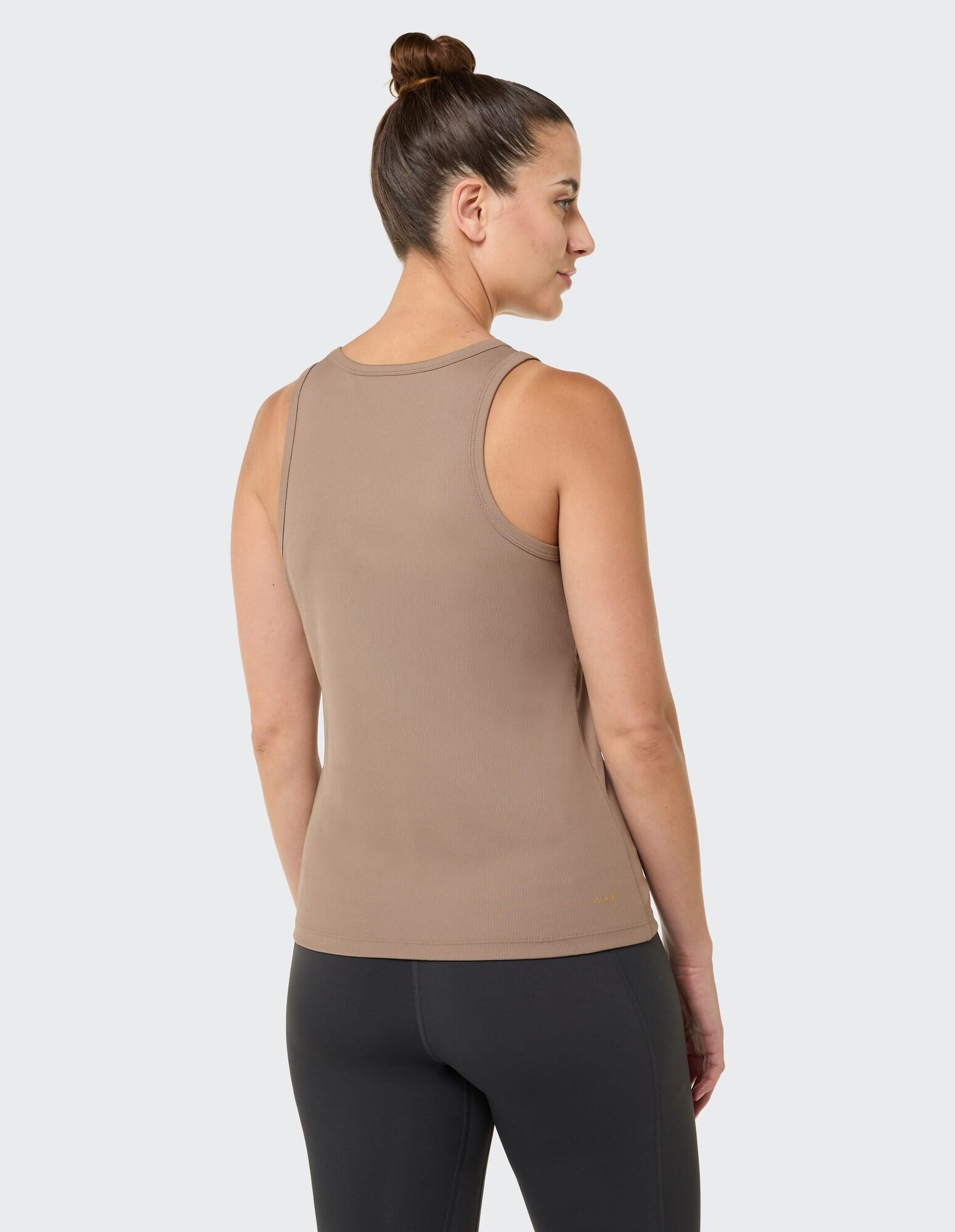 Rückansicht einer Frau in einem braunen Tanktop und schwarzen Leggings, die einen lässigen Stil zur Schau stellt.