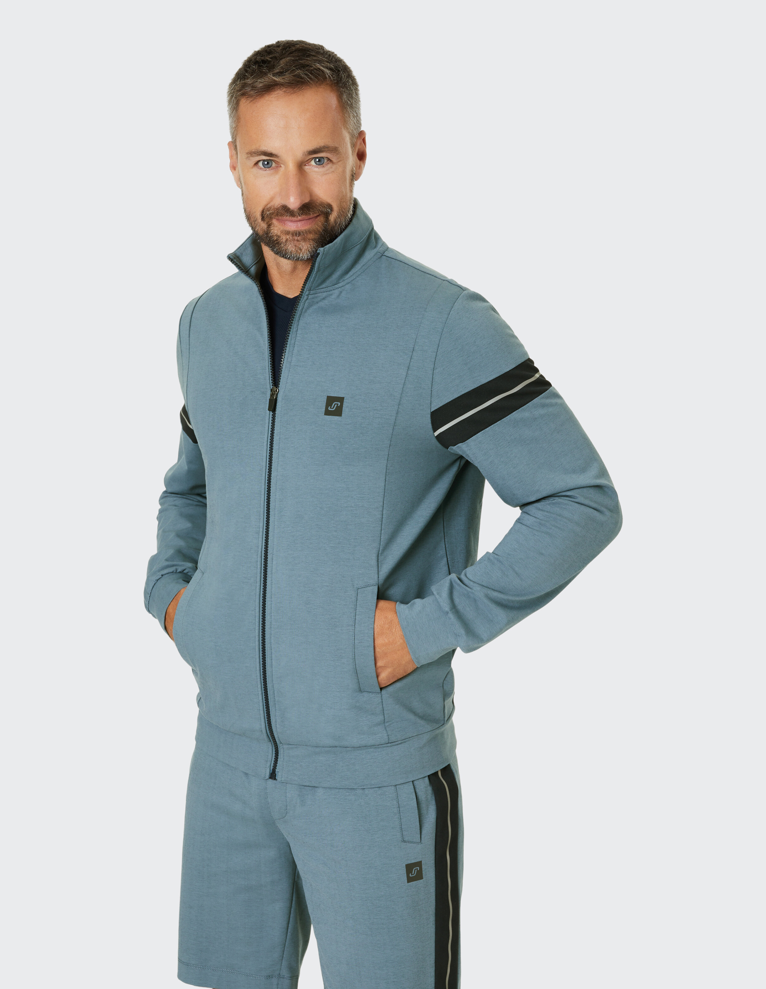 Blaue Trainingsjacke mit hohem Kragen, Reißverschluss, schwarzen Streifen auf den Ärmeln und elastischen Bündchen.