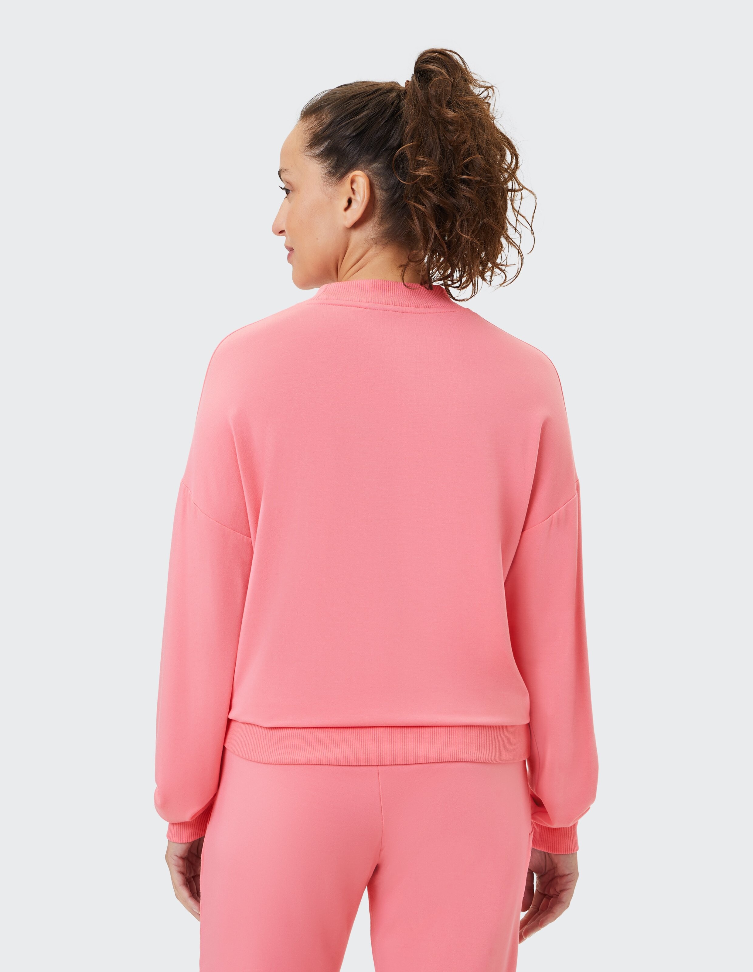 Frau trägt ein gemütliches rosafarbenes Freizeit-Sweatshirt mit geripptem Saum, Rückansicht.