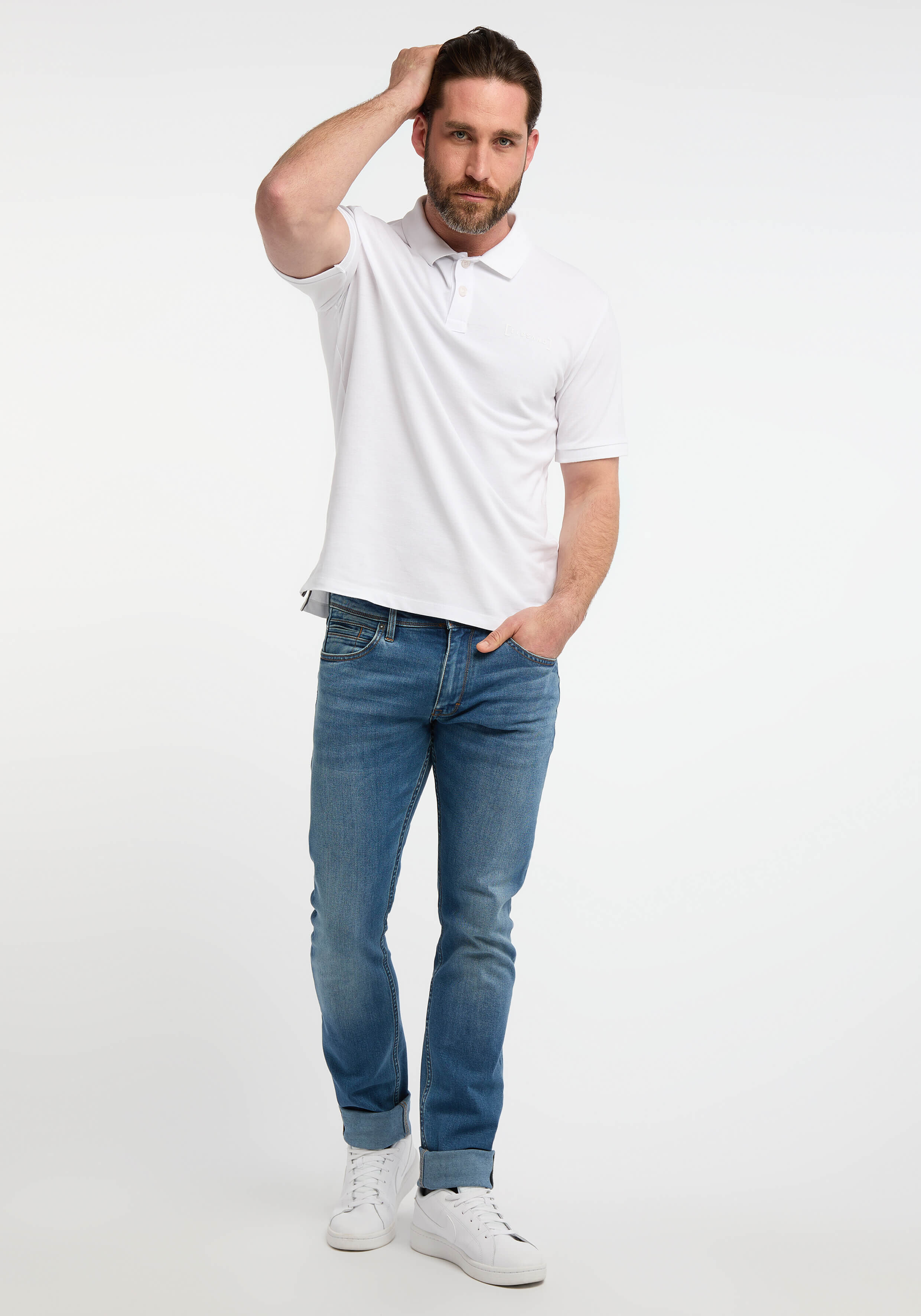 Mann in einem weißen Poloshirt und blauen Jeans, gestylt für Freizeitkleidung.