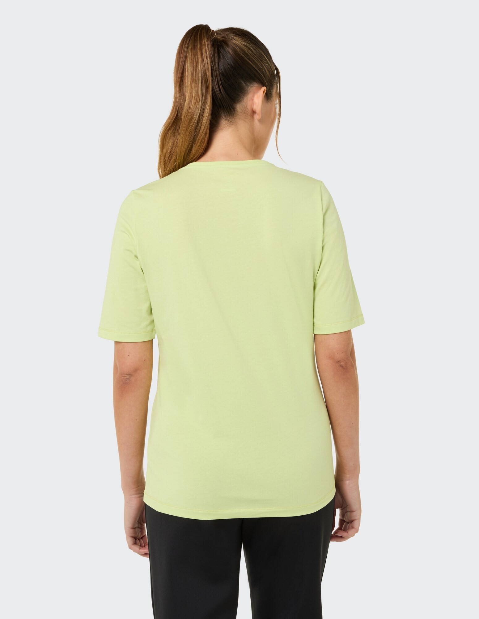 Rückansicht einer Frau, die ein hellgrünes Freizeit-T-Shirt mit kurzen Ärmeln trägt.