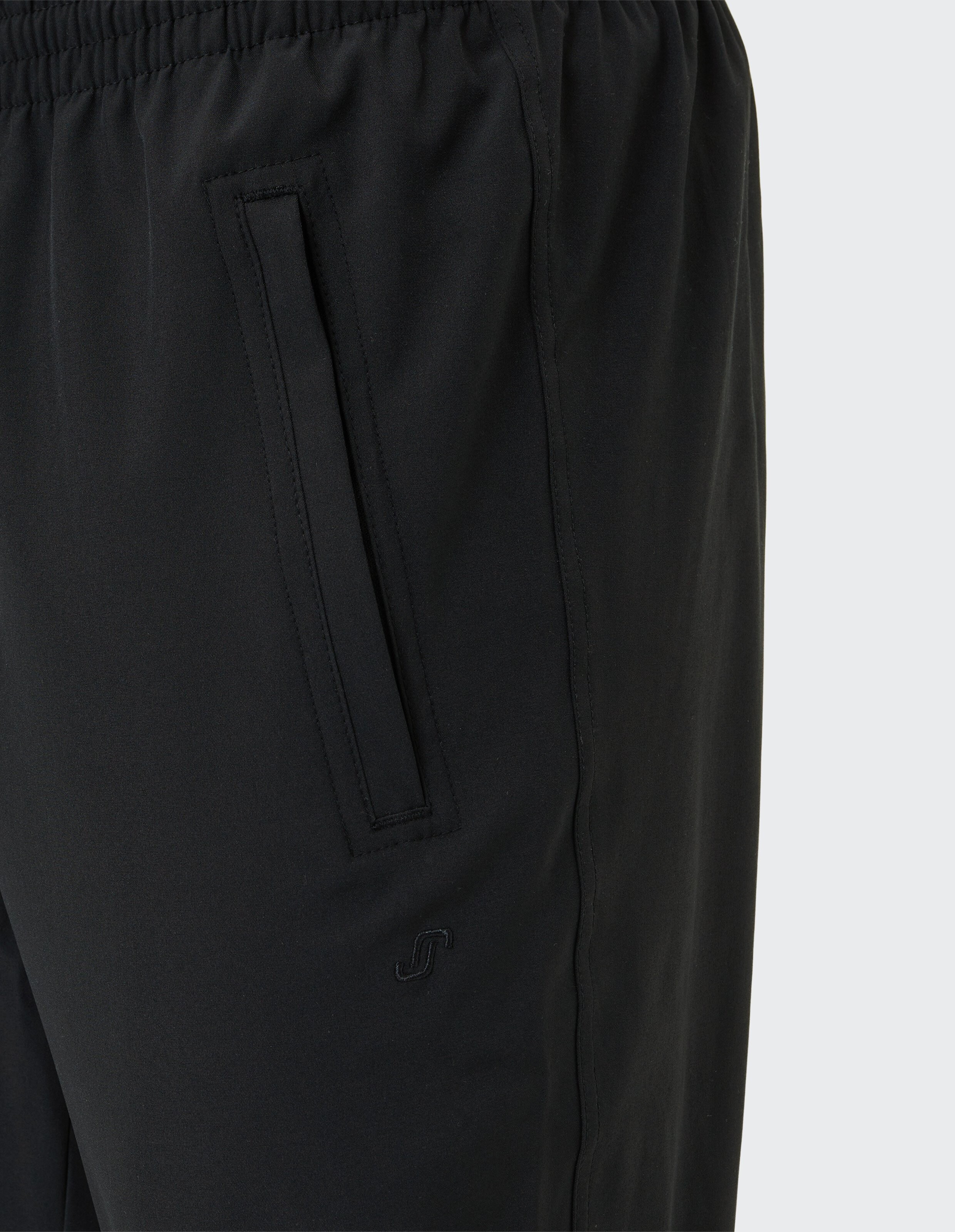 Nahaufnahme einer schwarzen Hose mit elastischem Bund und einer schrägen Tasche auf der rechten Seite, darauf ein kleines Logo.
