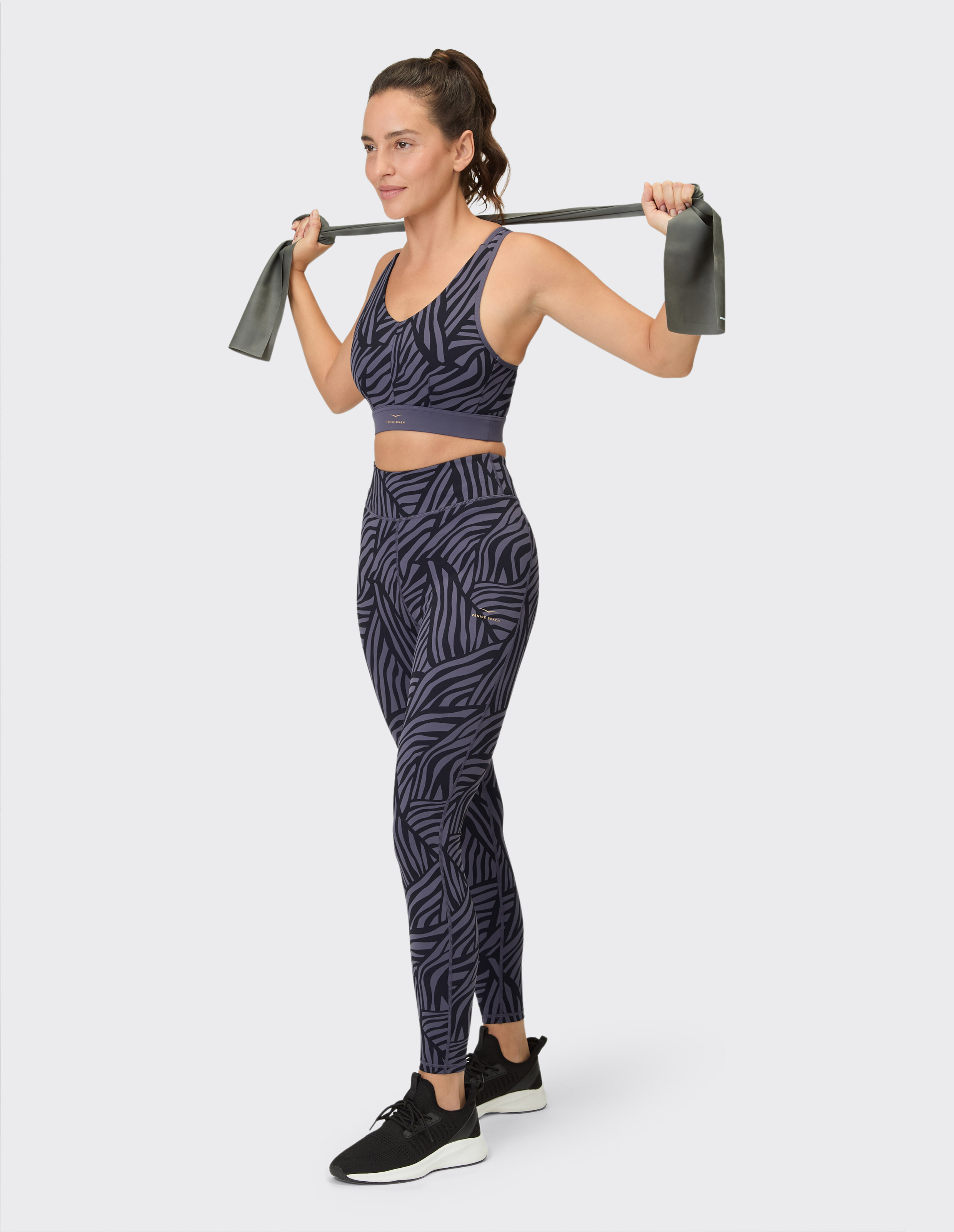Frau in gemustertem Sport-BH und Leggings trainiert mit einem Widerstandsband.