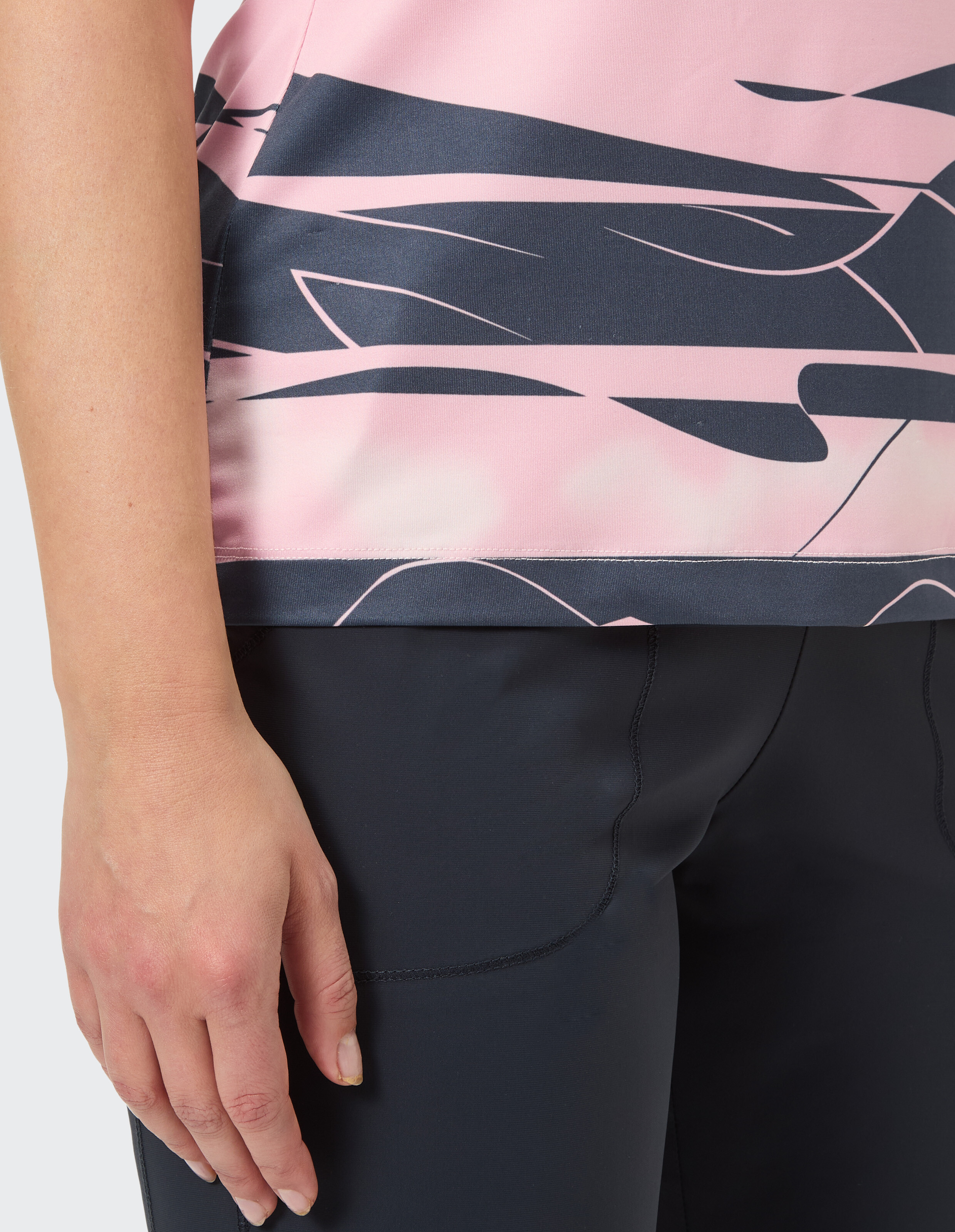 Nahaufnahme der Hand einer Frau auf einem rosa und dunkelblau gemusterten Freizeitoberteil und einer dunklen Hose.