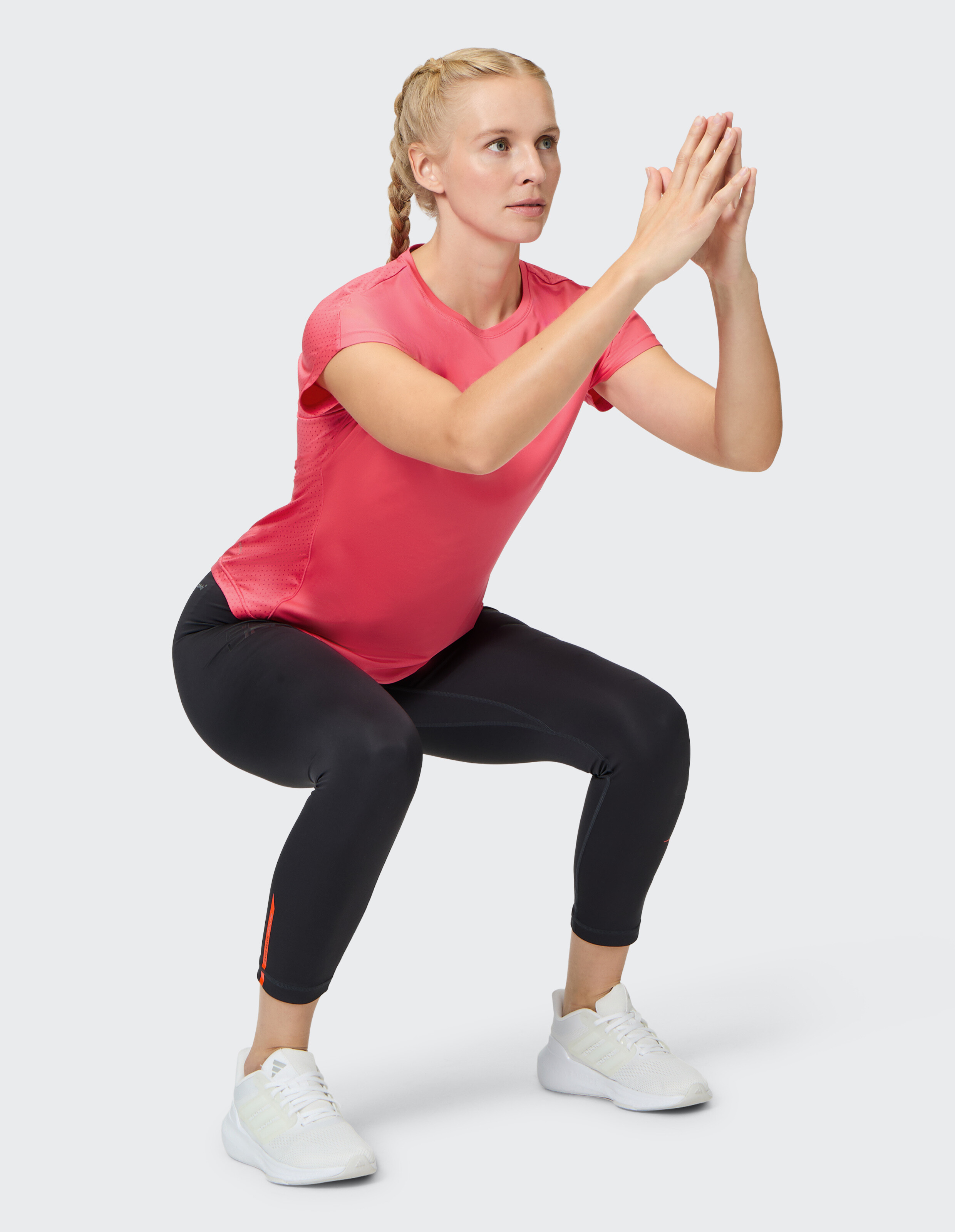Frau in einem rosa T-Shirt und schwarzen Leggings macht eine Kniebeuge zum Training.