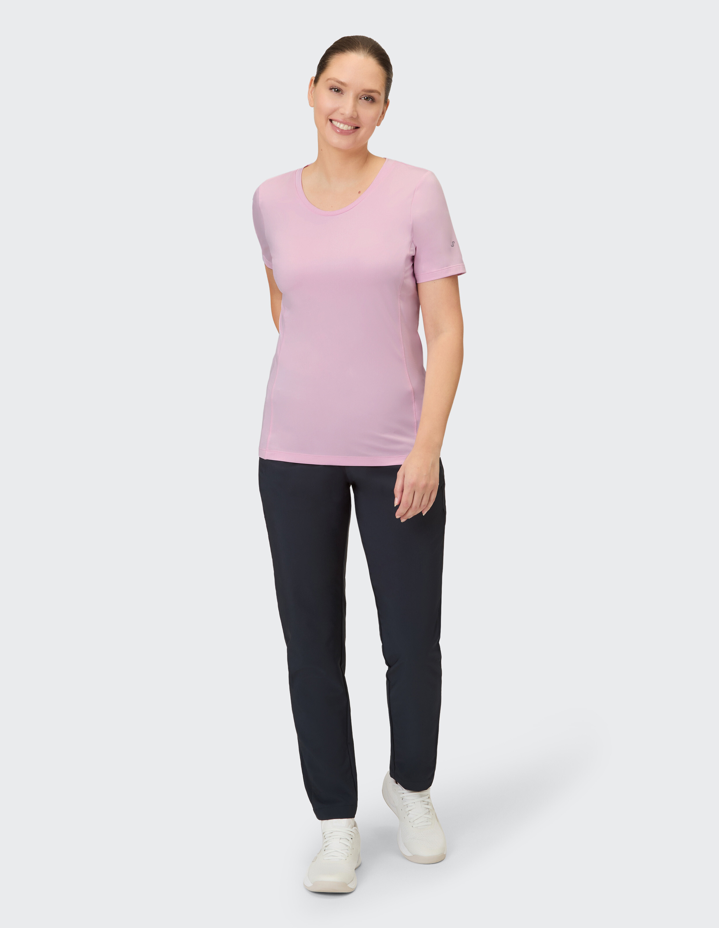 Eine Frau trägt ein hellrosa kurzärmeliges T-Shirt und eine schwarze Hose.