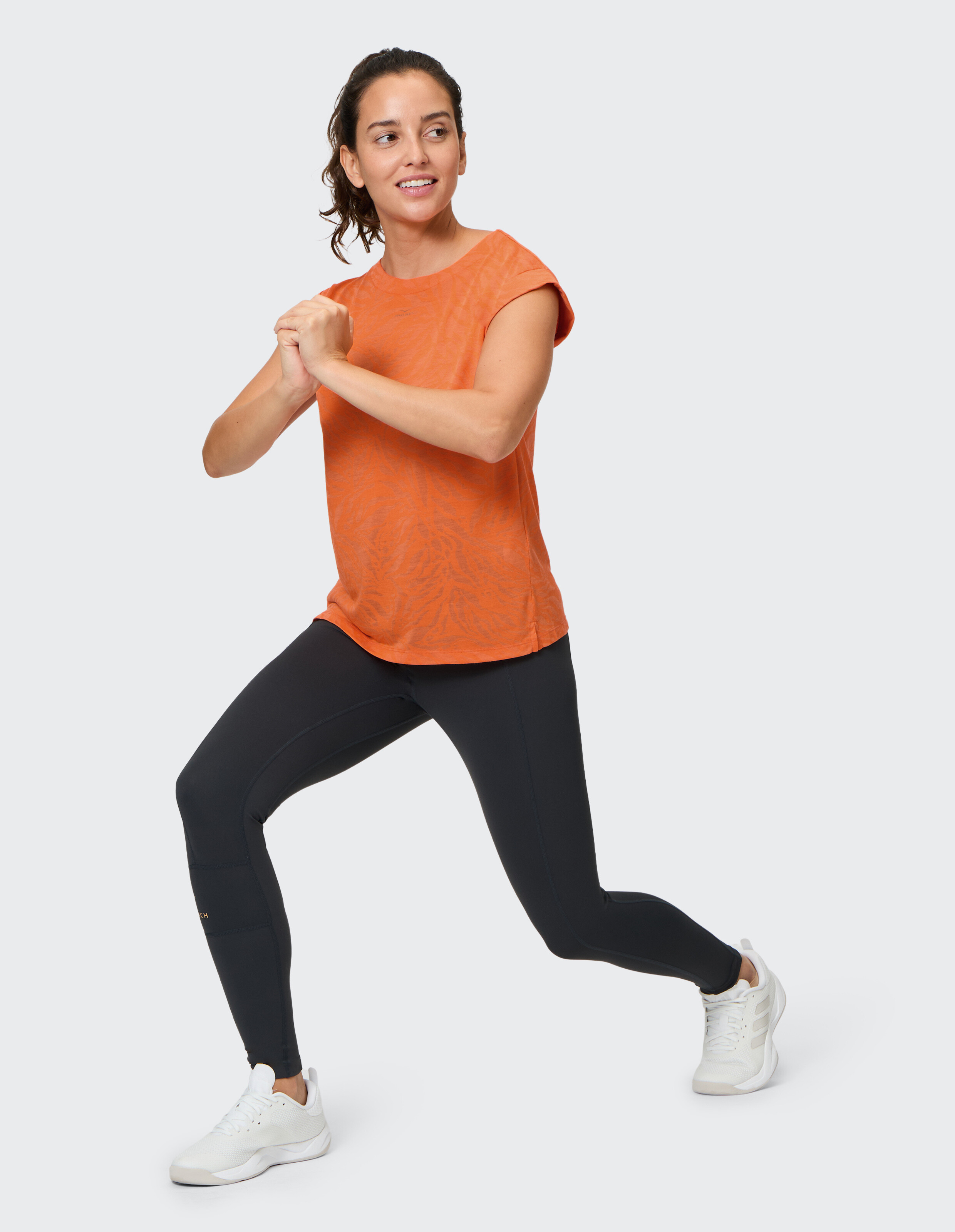 Frau trägt ein orangefarbenes Venice Beach Tirara-Kurzarmhemd und schwarze Leggings.