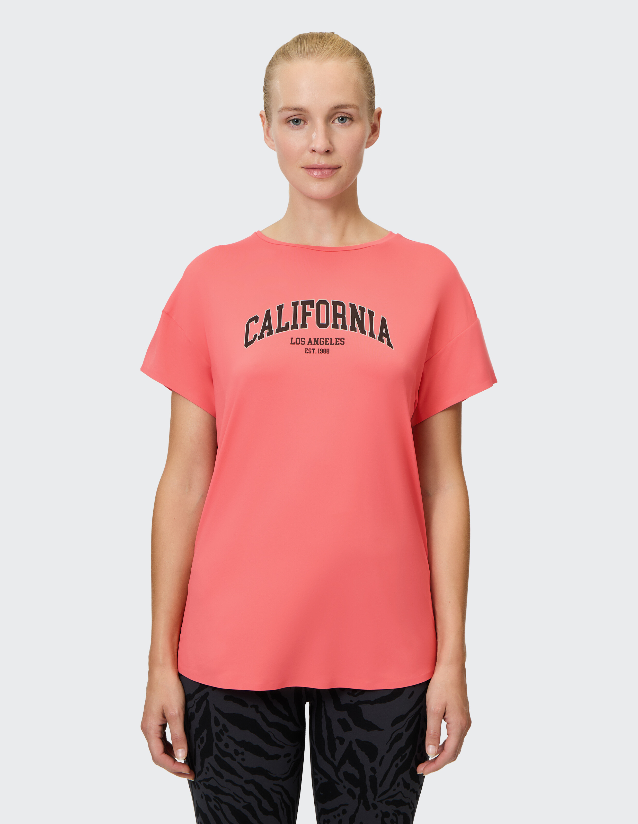 Frau trägt ein korallenrosa Freizeit-T-Shirt mit kalifornischem Grafikdruck.
