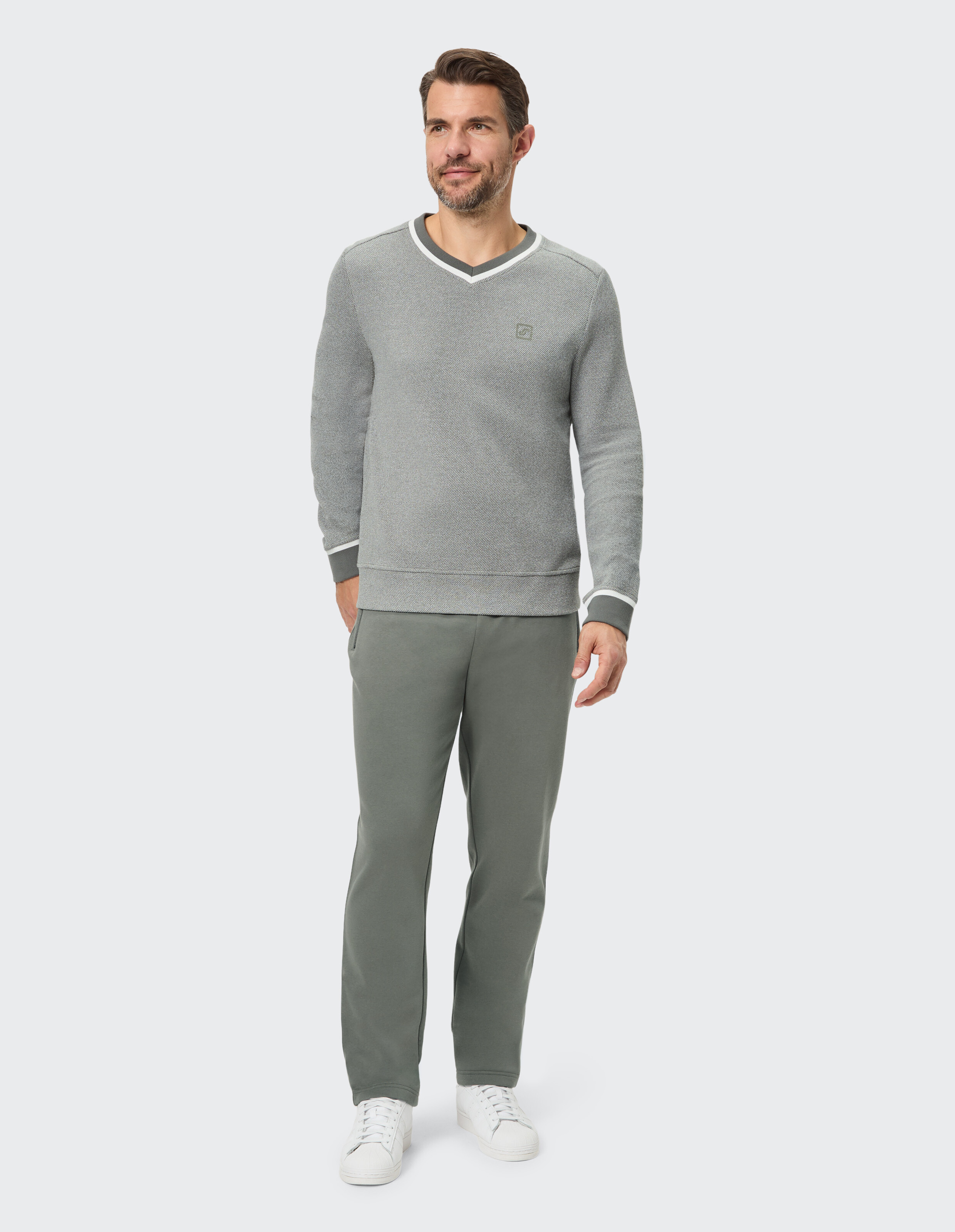 Mann in einem grauen Pullover mit V-Ausschnitt und grüner Hose, der lässigen Komfort zur Schau stellt.
