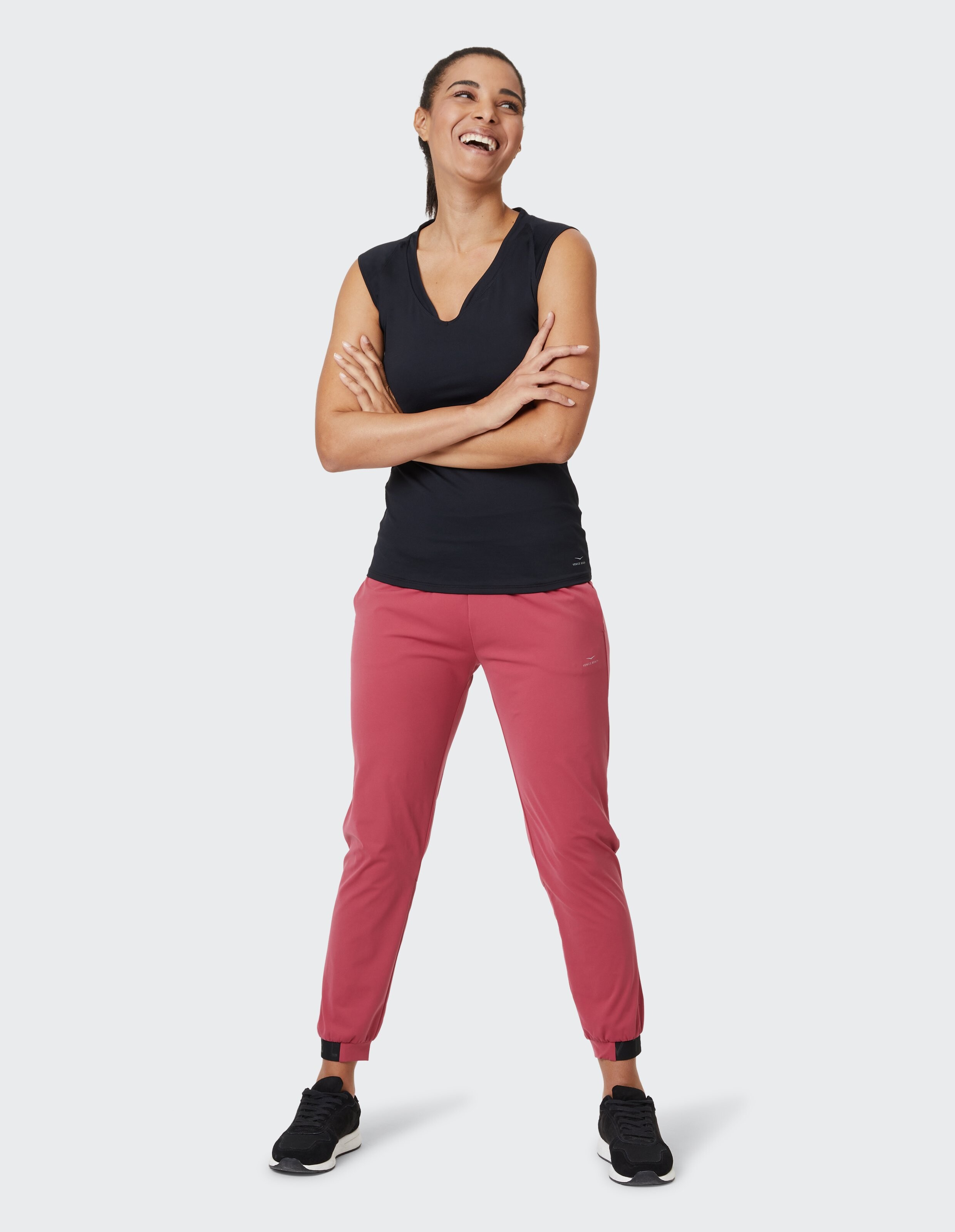 Frau trägt ein schwarzes ärmelloses Oberteil und rosa Freizeit-Jogginghosen für einen bequemen Look.
