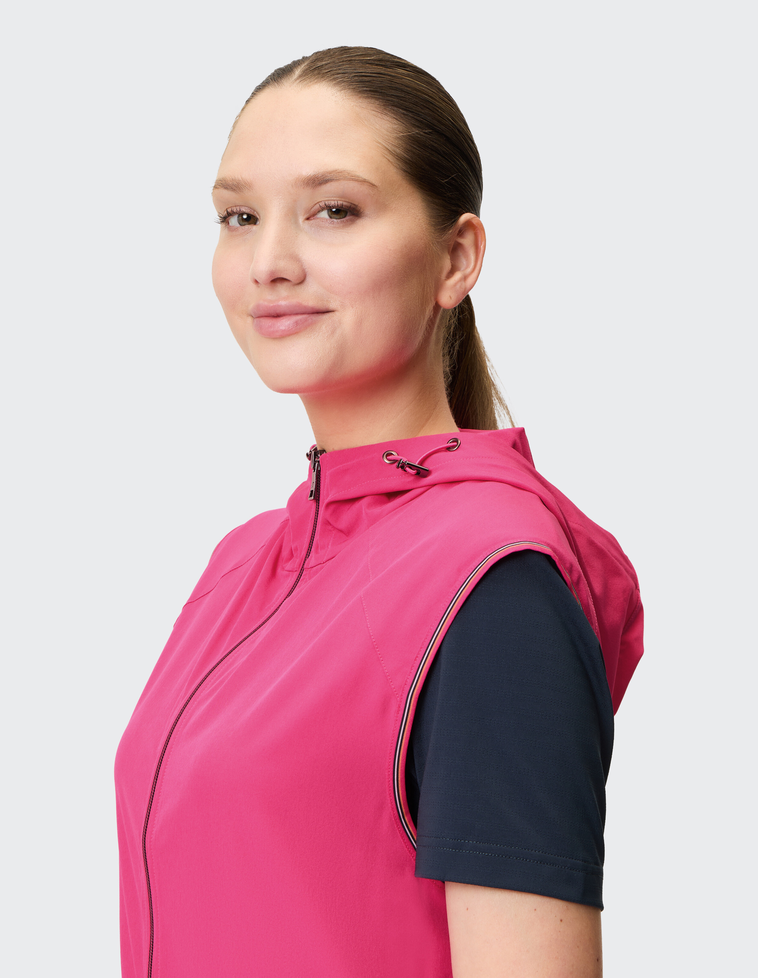 Das Model präsentiert eine ärmellose rosa Weste über einem dunkelblauen T-Shirt, perfekt für Freizeitausflüge oder zum Faulenzen.