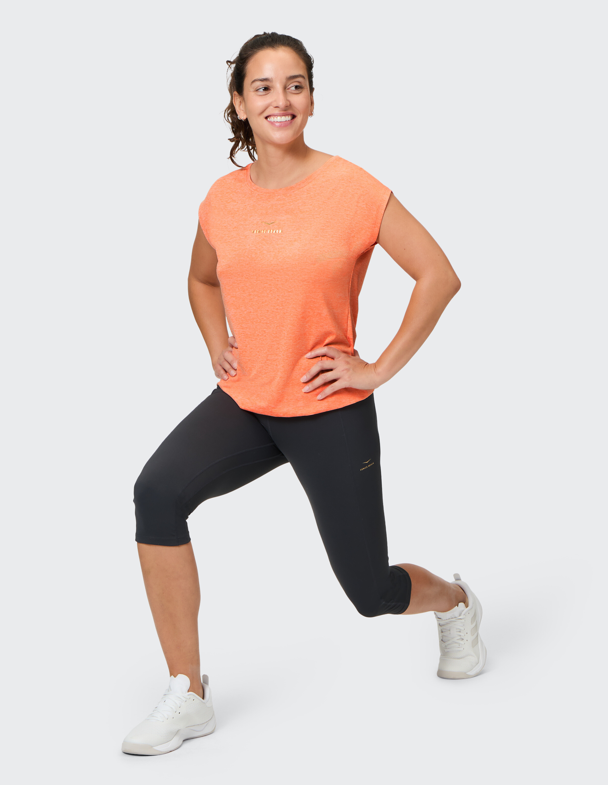 Frau in orangefarbenem Top und schwarzen Leggings im lässigen Activewear-Stil.