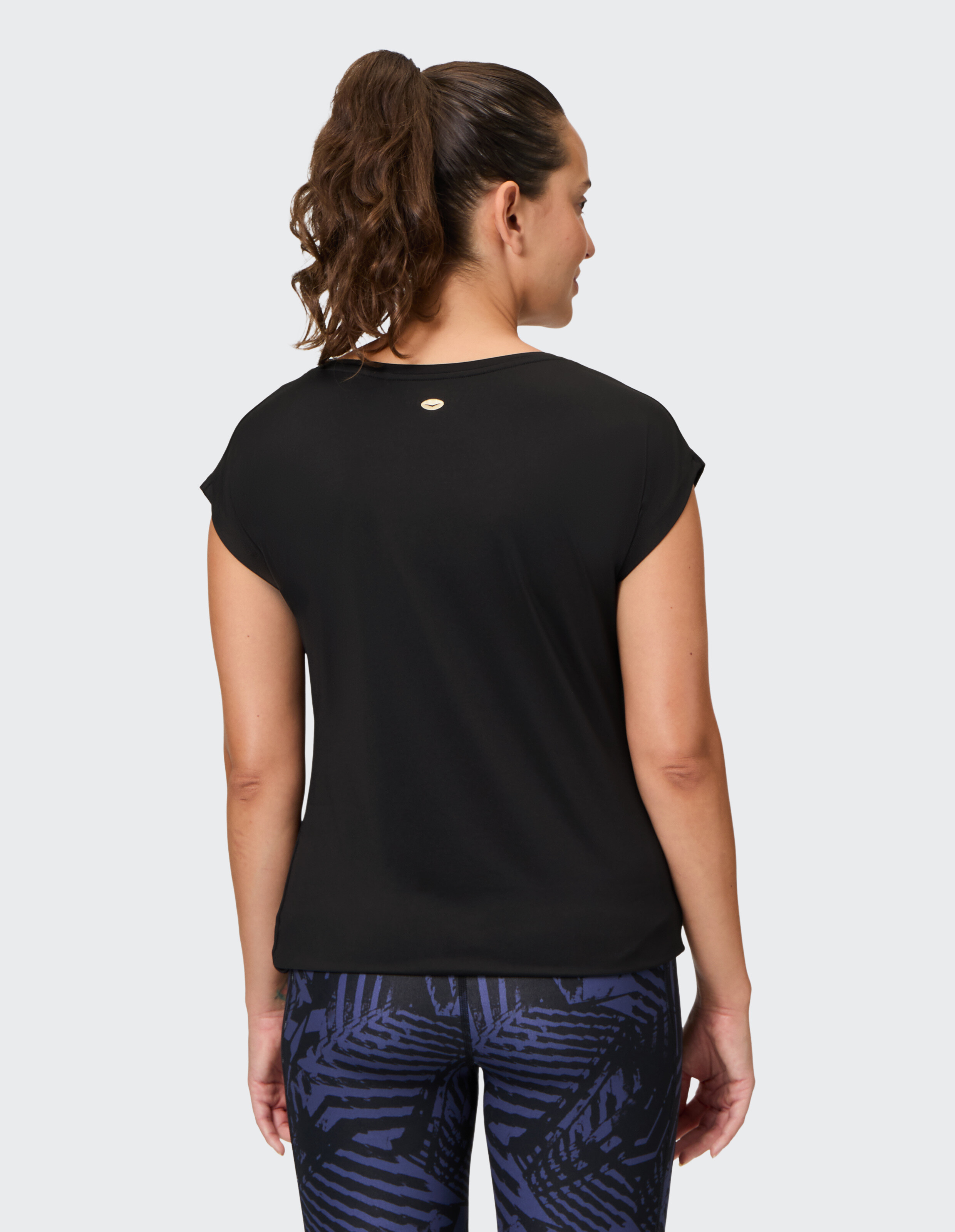 Rückansicht einer Frau in einem schwarzen Freizeittop gepaart mit gemusterten Leggings.