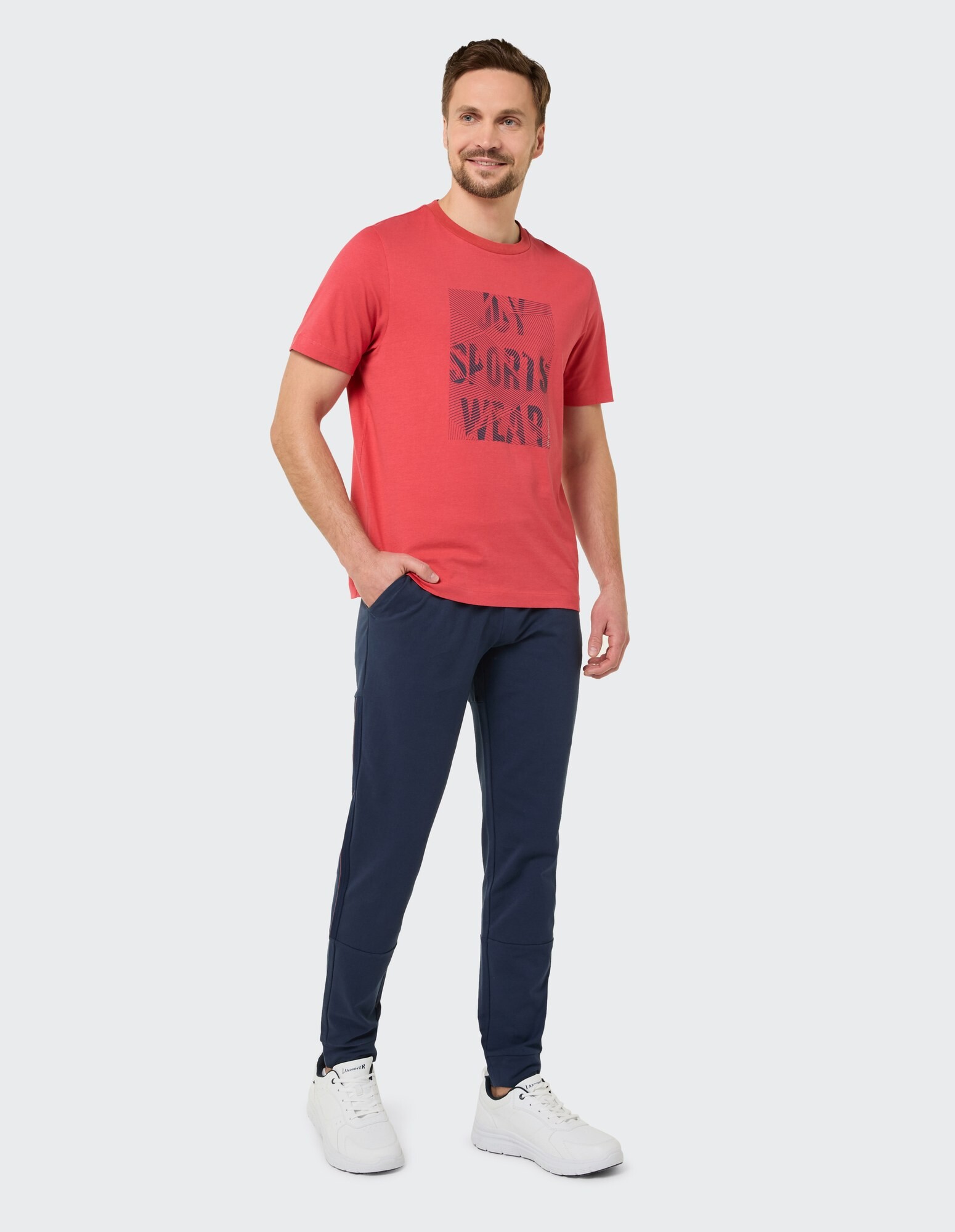 Mann in einem roten grafischen T-Shirt und dunkelblauen Jogginghosen, gestylt für Freizeitkleidung.