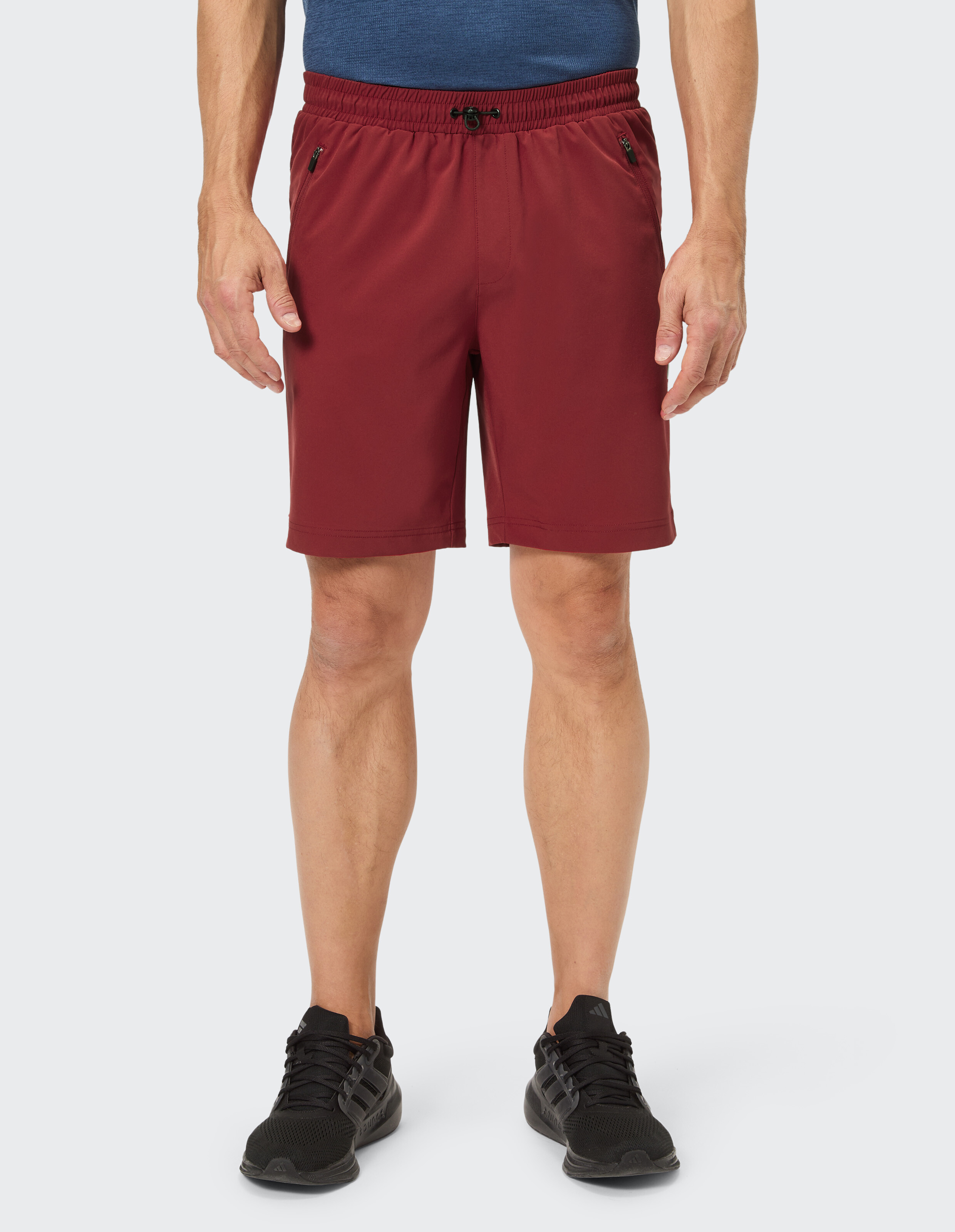 Mann trägt rote Shorts mit Kordelzug und Reißverschlusstaschen, dazu ein blaues T-Shirt und schwarze Sportschuhe.