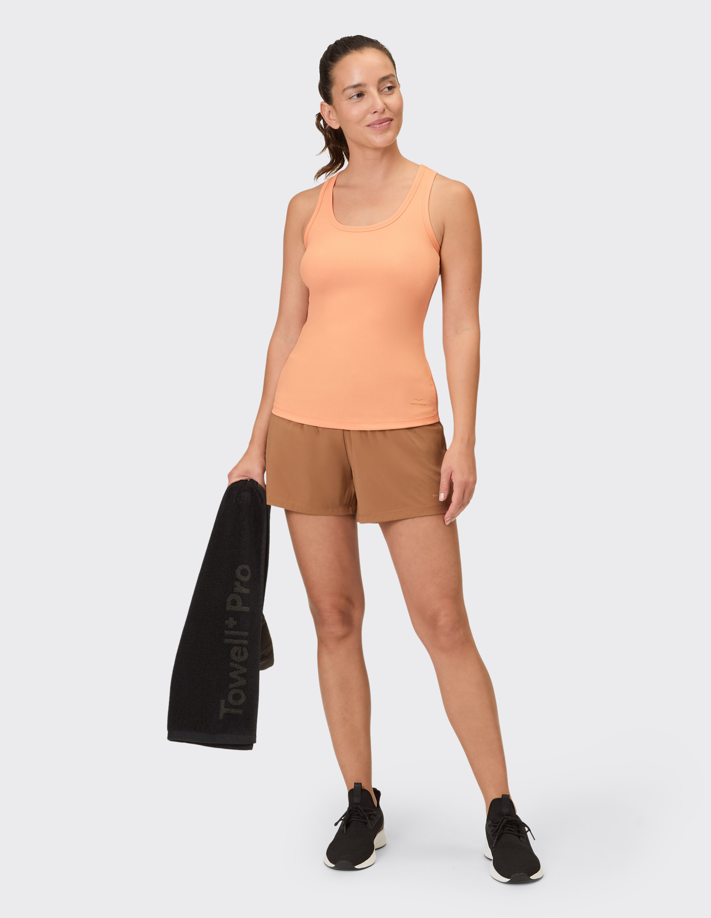Frau trägt ein pfirsichfarbenes Venice Beach Brenda-Tanktop und braune Freizeitshorts.