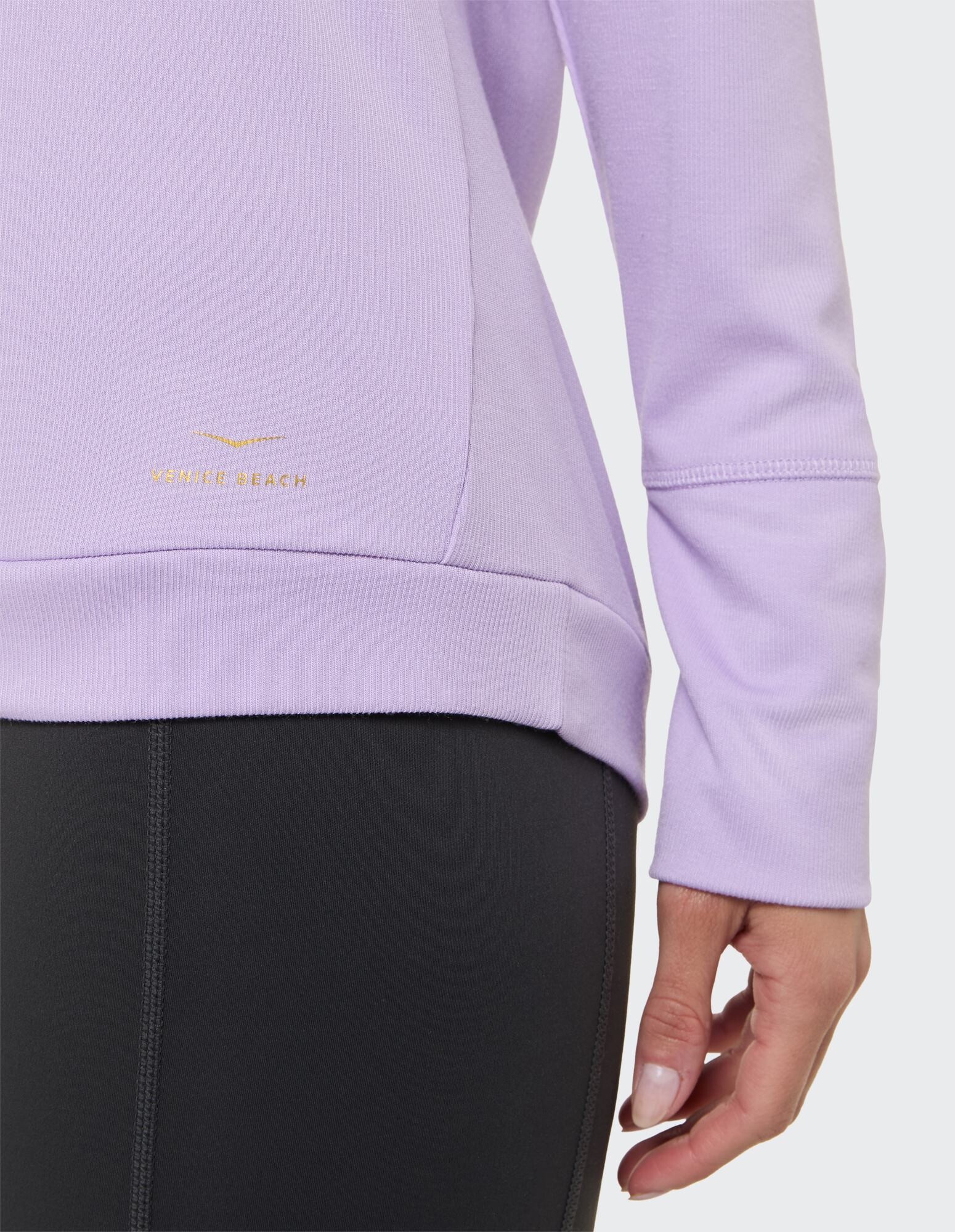 Nahaufnahme eines fliederfarbenen Langarm-Tops mit stylischem Schnitt und Logo-Detail.