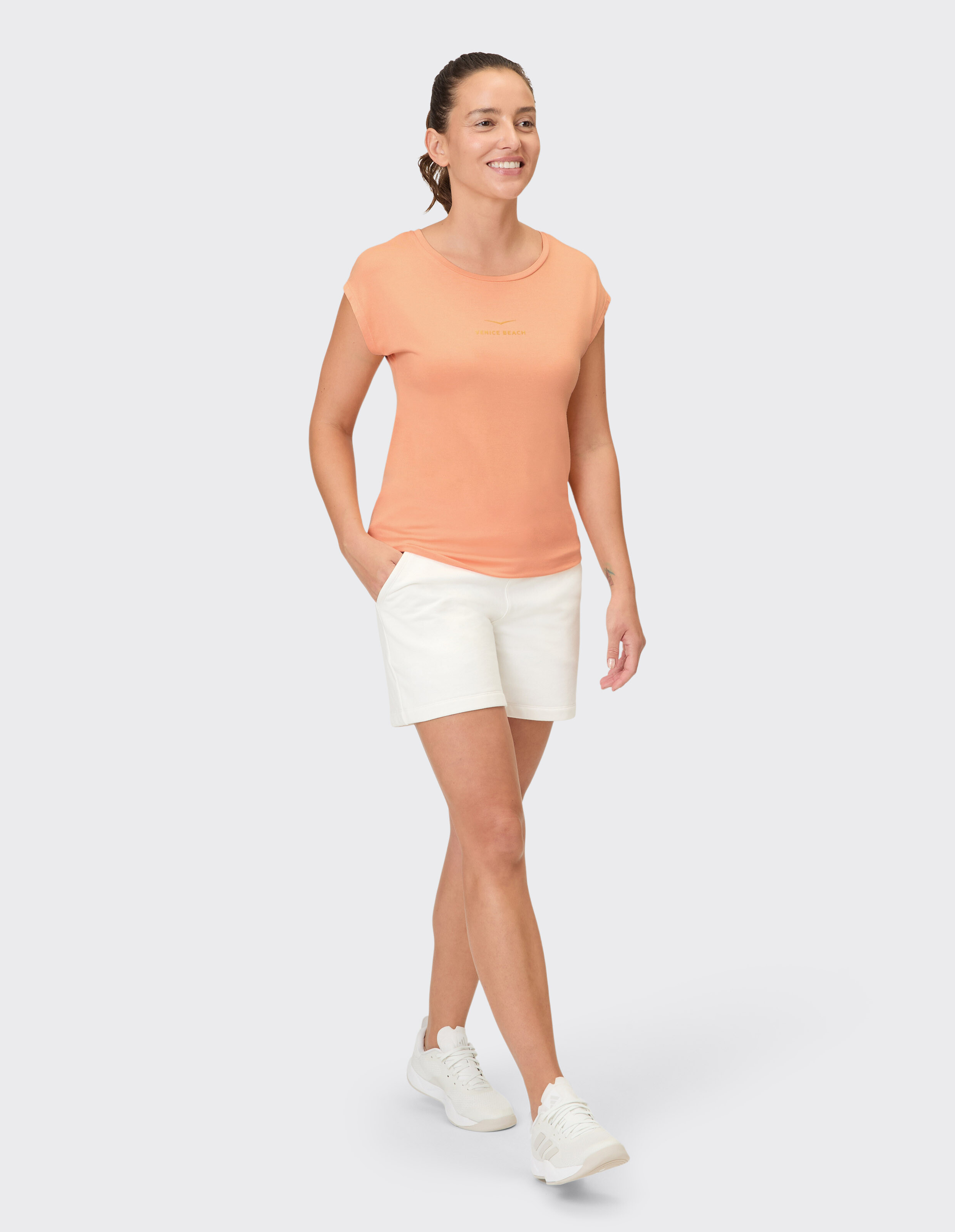 Frau trägt ein pfirsichfarbenes T-Shirt und weiße Shorts für einen gemütlichen, lässigen Sommerlook.