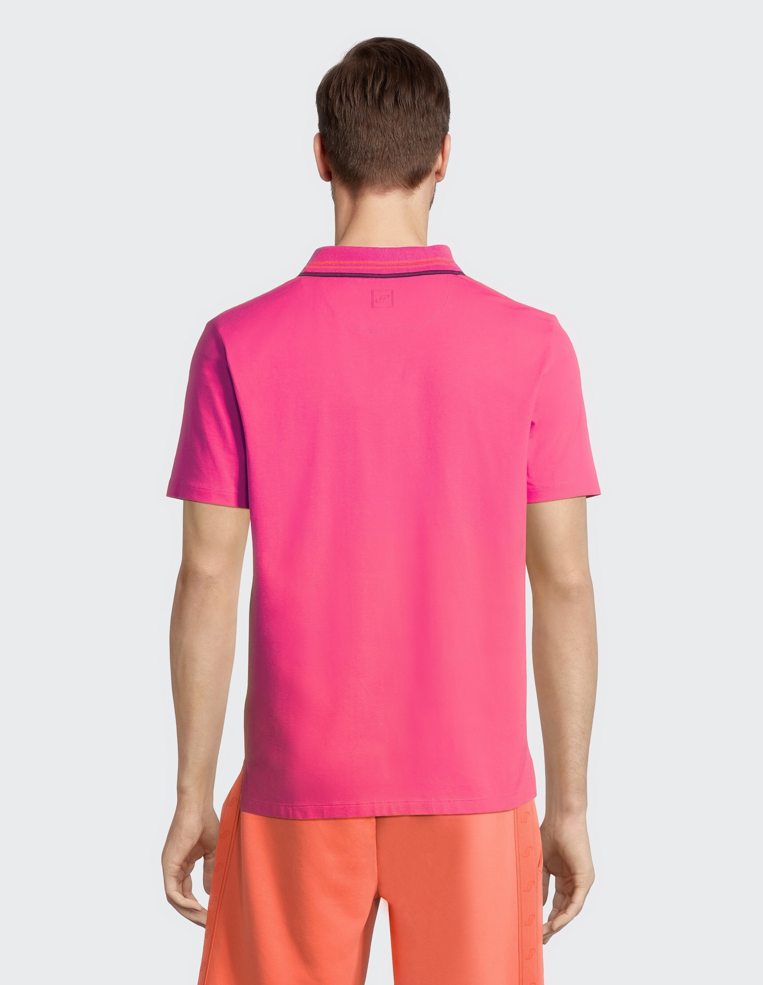 Rückansicht eines Mannes, der ein leuchtend rosa Poloshirt und orangefarbene Shorts trägt.