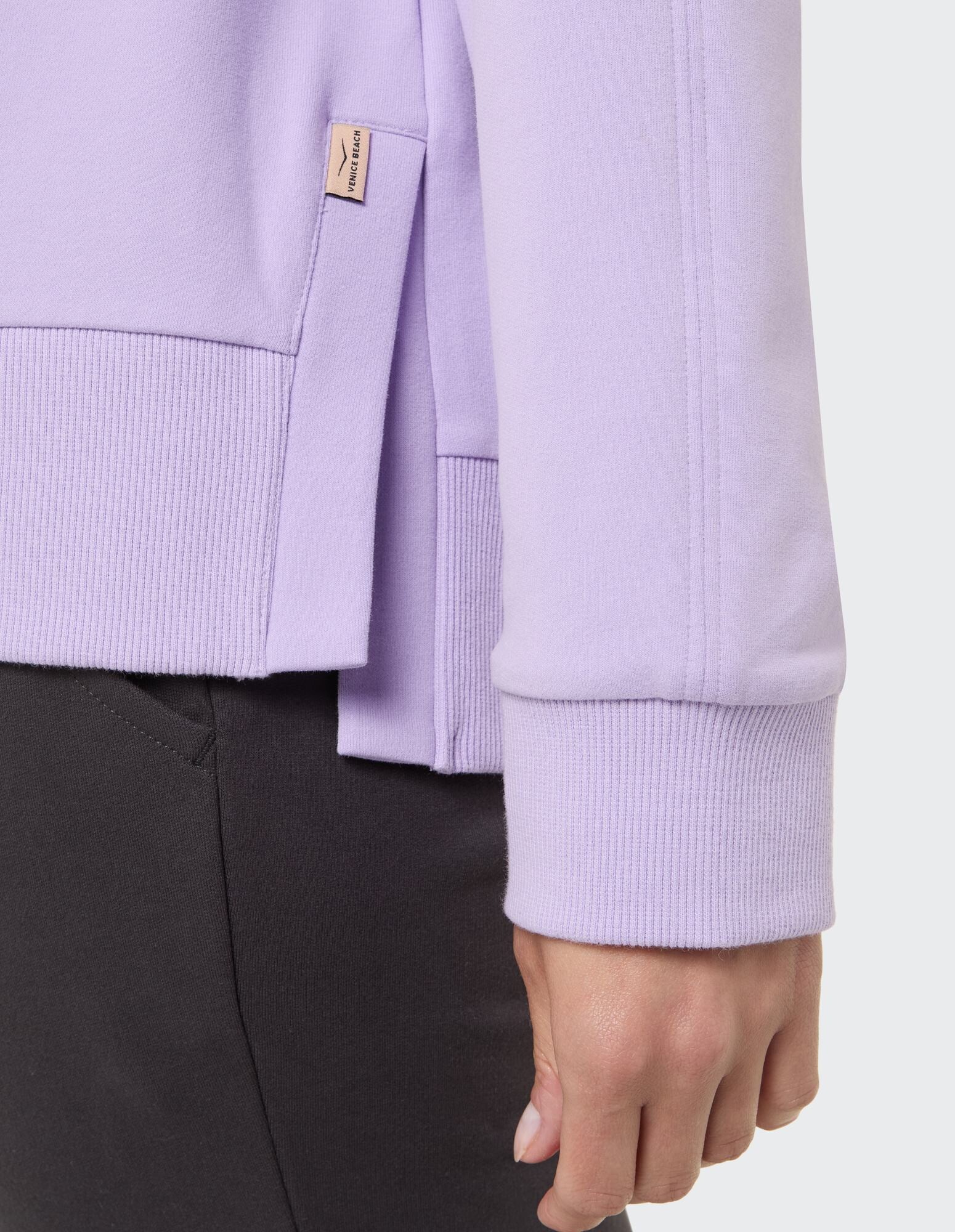 Nahaufnahme eines lila Sweatshirts mit gerippten Bündchen und seitlichen Schlitzdetails.