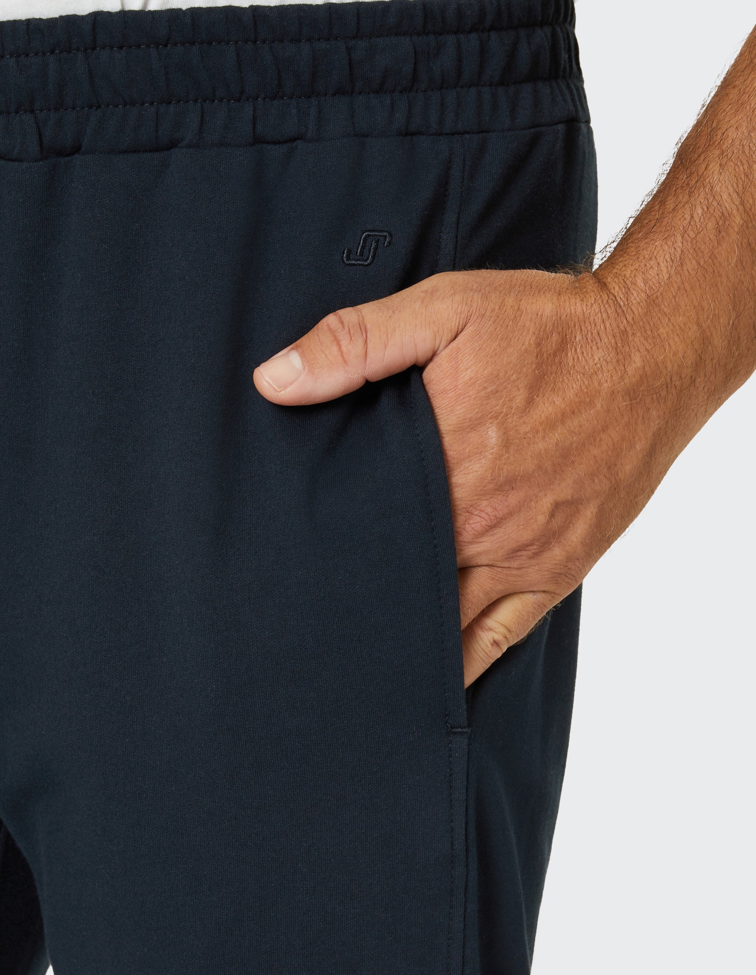 Nahaufnahme einer Hand in einer dunklen Sporthose mit elastischem Bund und kleinem Logo auf der Seite.