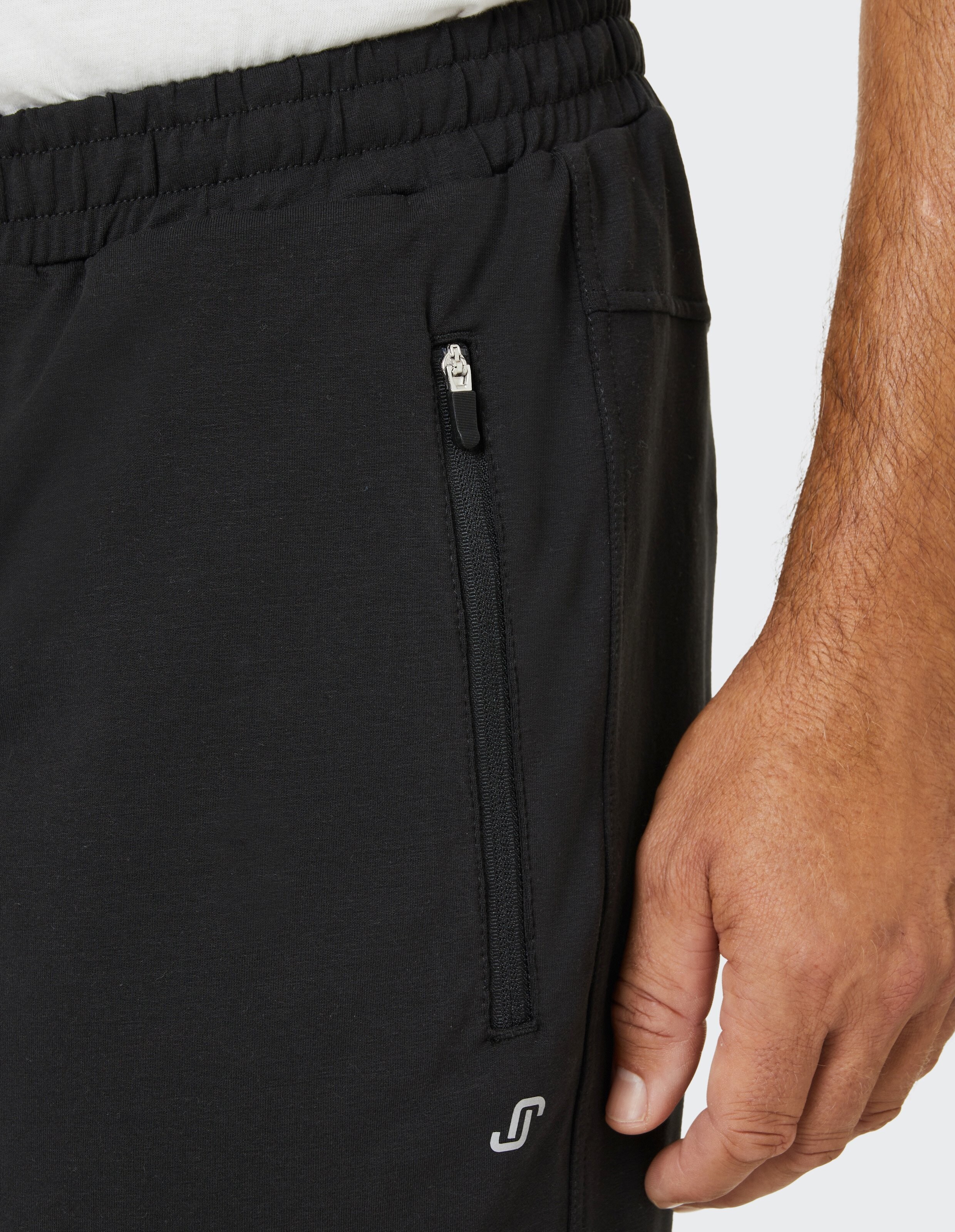Nahaufnahme eines Arms in einer schwarzen Hose mit elastischem Bund und seitlichem Reißverschluss sowie kleinem Logo auf der Tasche.