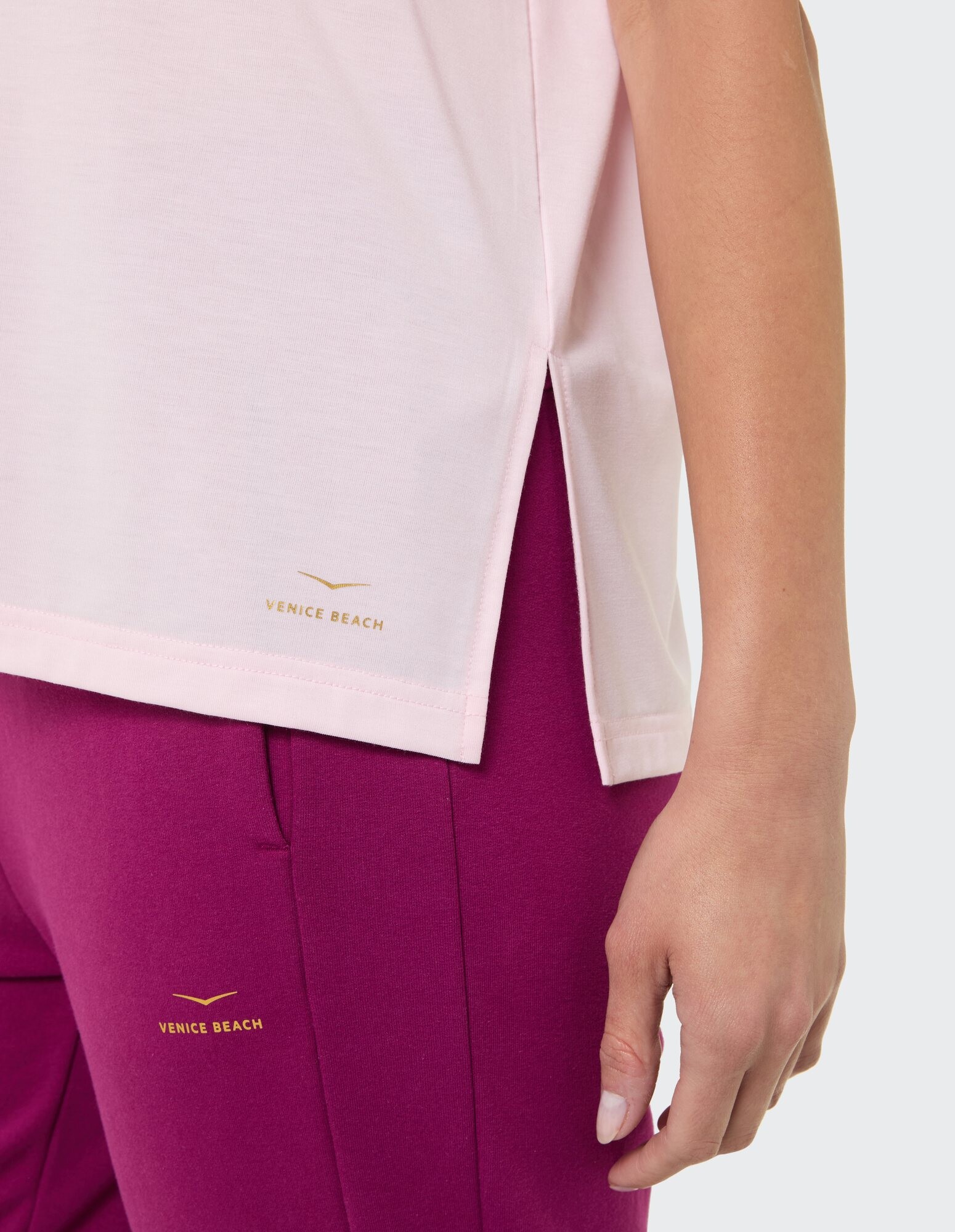 Nahaufnahme eines rosa Oberteils mit Seitenschlitzen gepaart mit einer lila Hose mit Venice Beach-Branding.