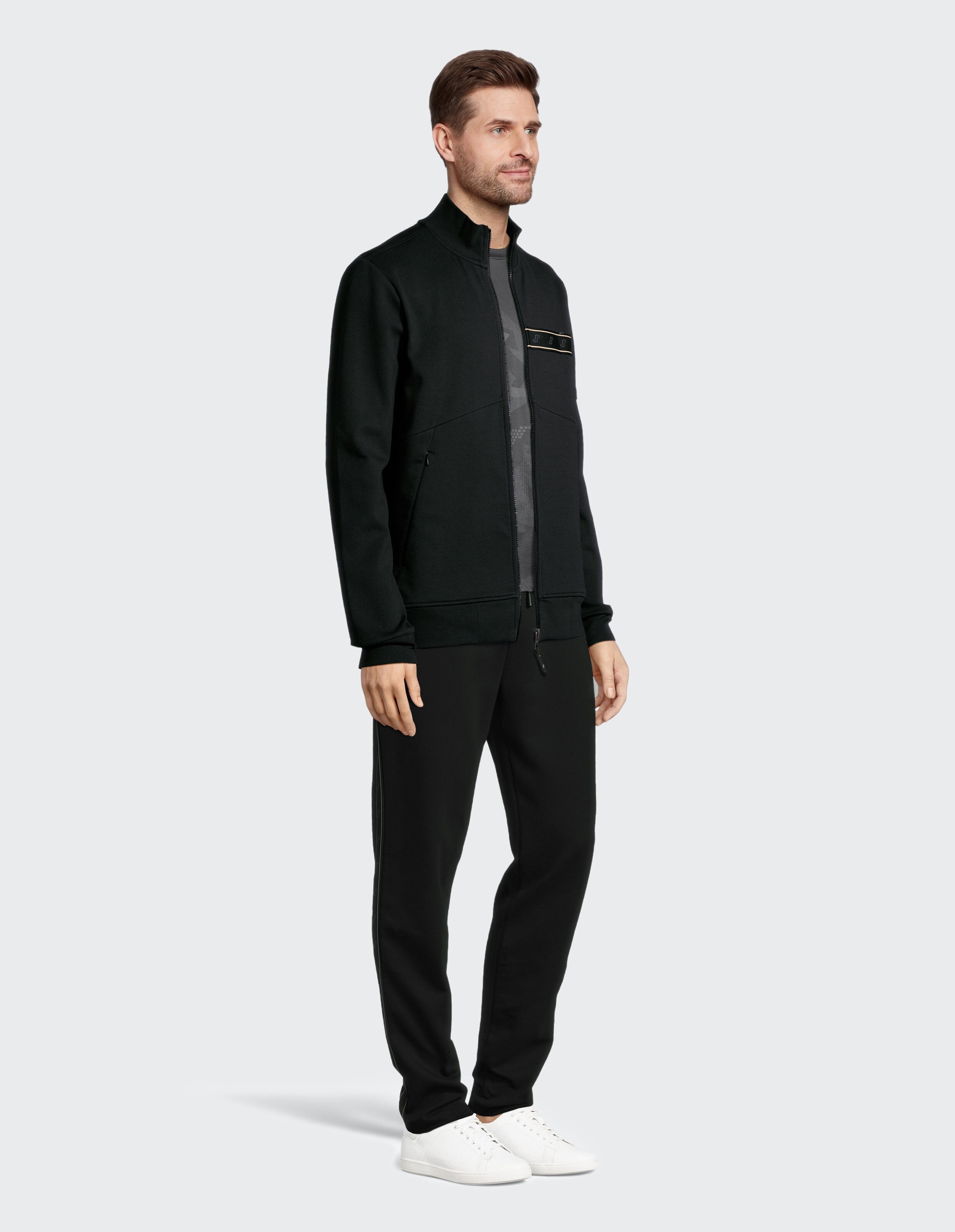 Mann in einer schwarzen Jacke mit Reißverschluss und passender Hose, lässig gestylt.