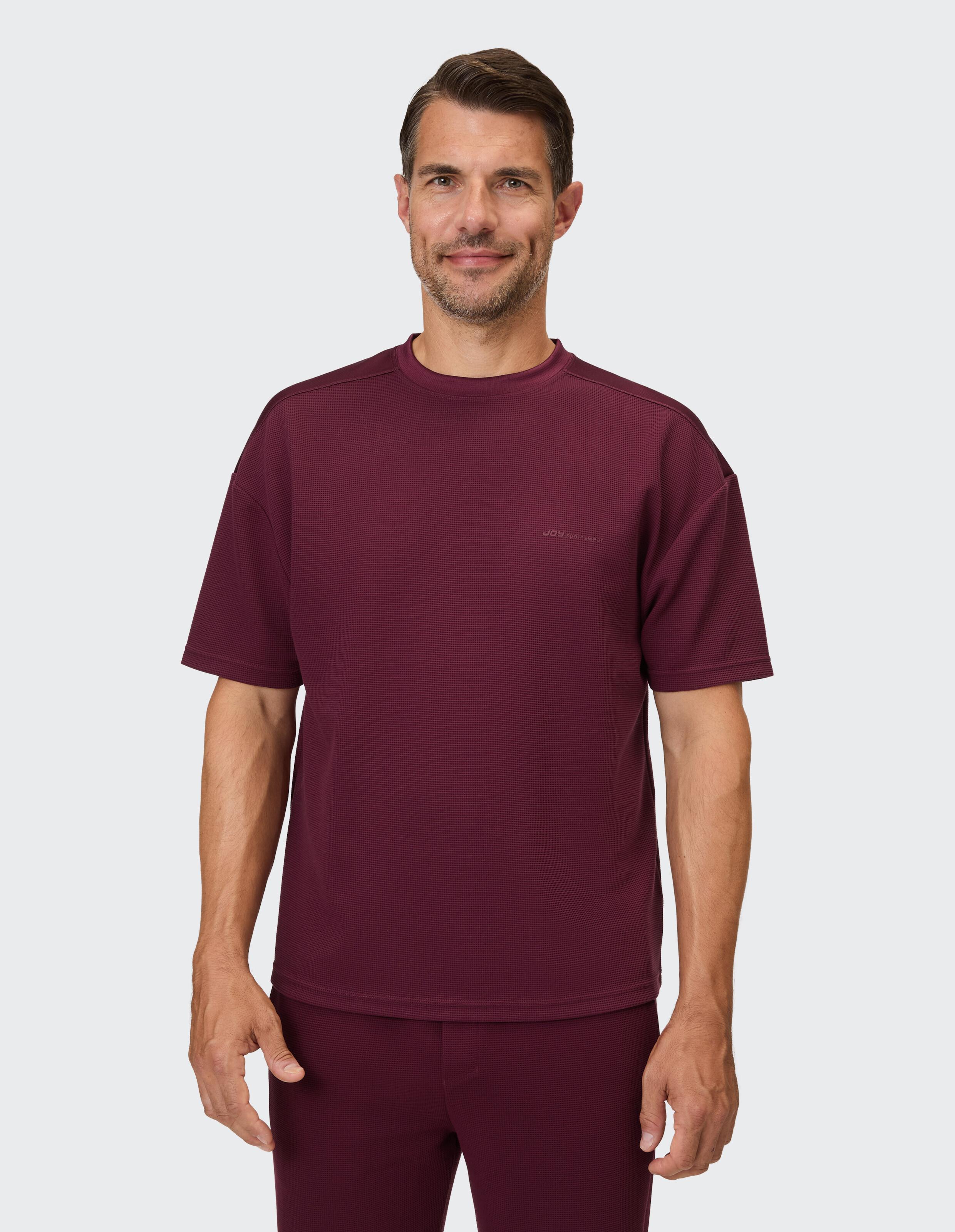 Ein Mann trägt ein weinrotes T-Shirt mit Waffelmuster und passender Hose.