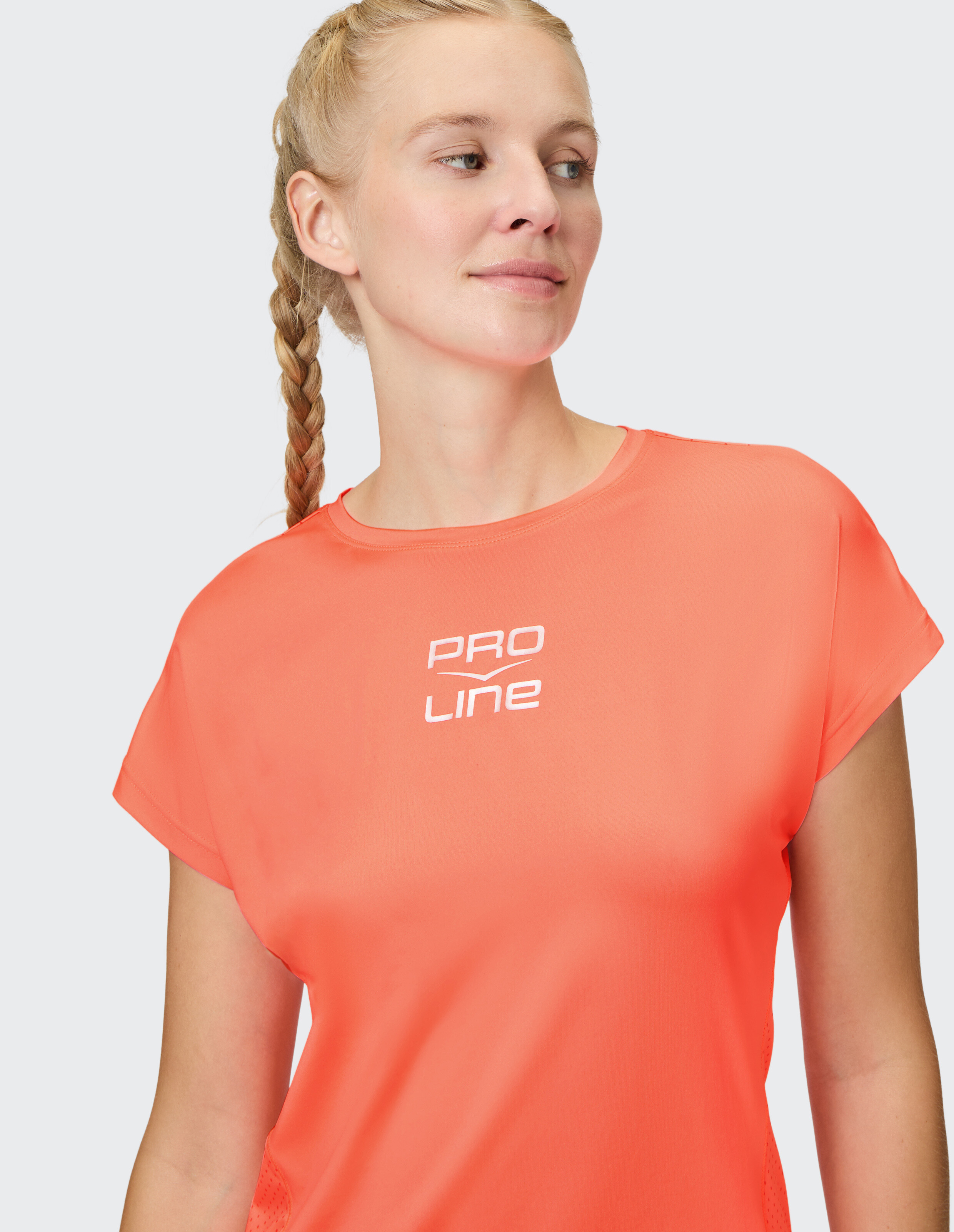 Frau in einem leuchtend orangefarbenen PROLINE-T-Shirt, das einen lässigen und sportlichen Stil unterstreicht.
