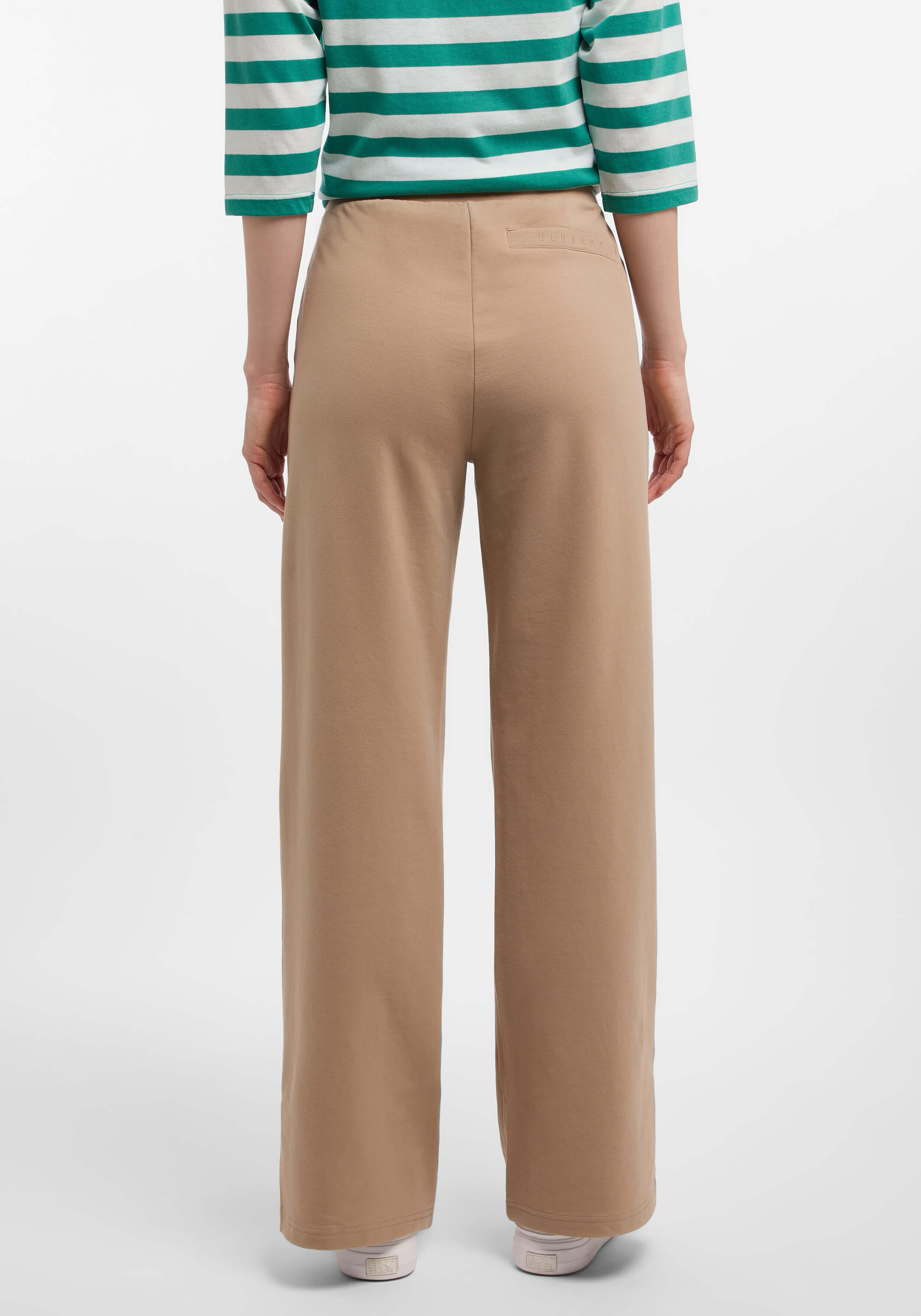 Rückansicht einer beigefarbenen Lounge-Hose mit weitem Bein, gepaart mit einem grün-weiß gestreiften Oberteil.