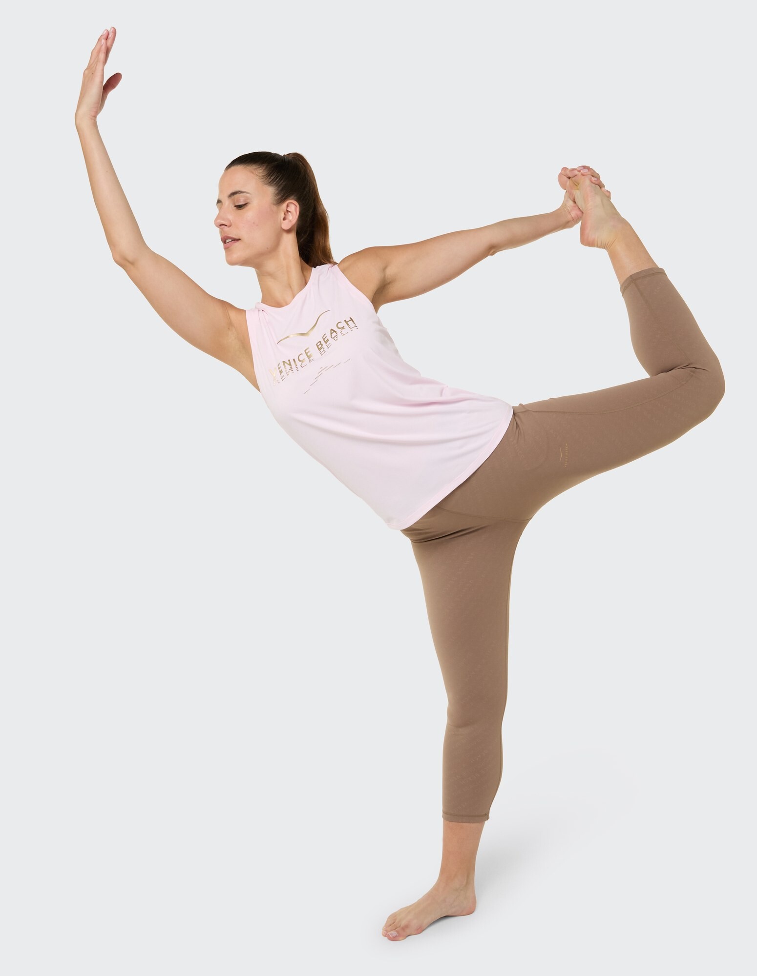 Frau macht Yoga in einem rosa Tanktop und braunen Leggings und demonstriert Flexibilität.