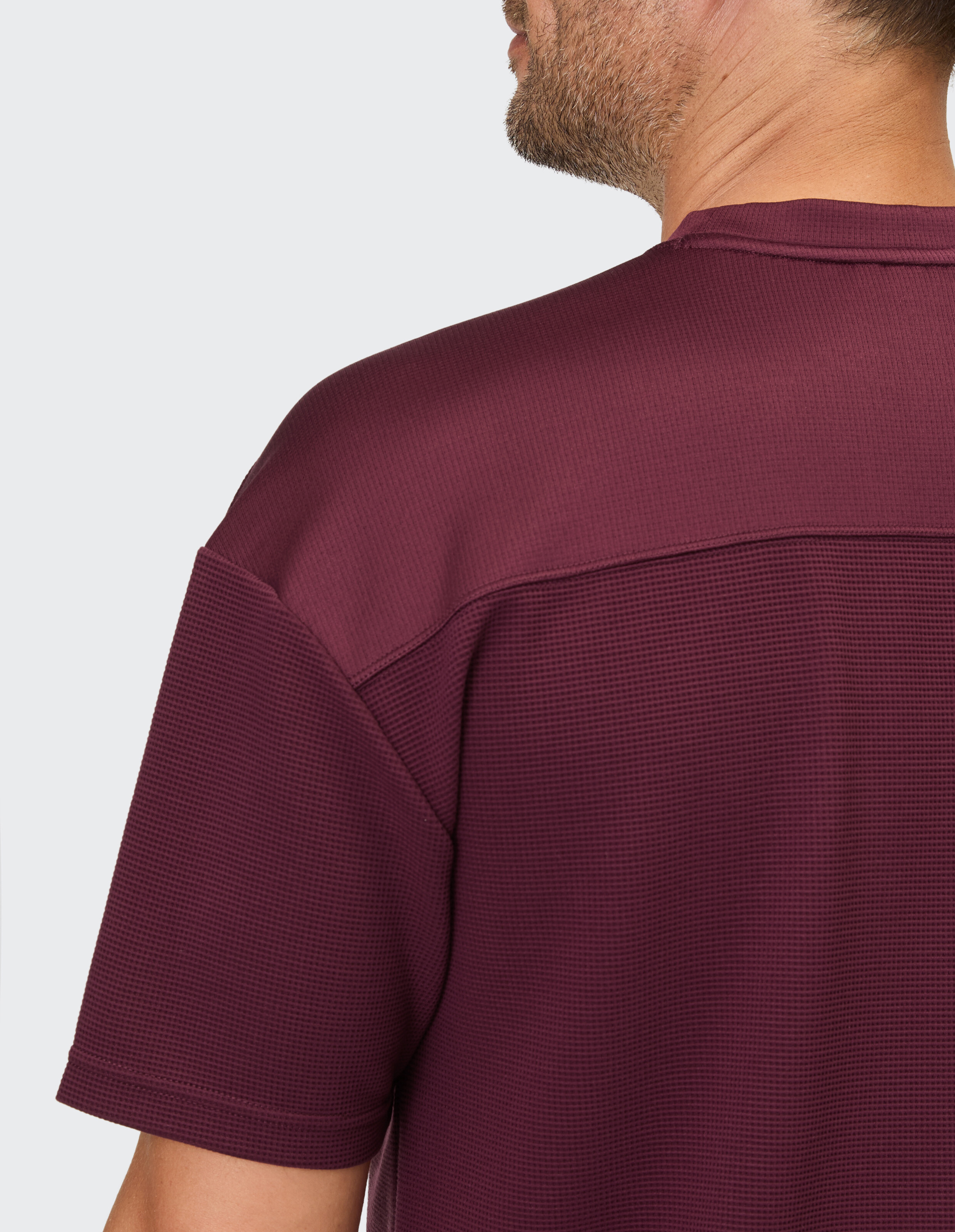 Ein Mann trägt ein bordeauxrotes T-Shirt mit Waffelmuster und einem glatten Paneel über den Schultern.