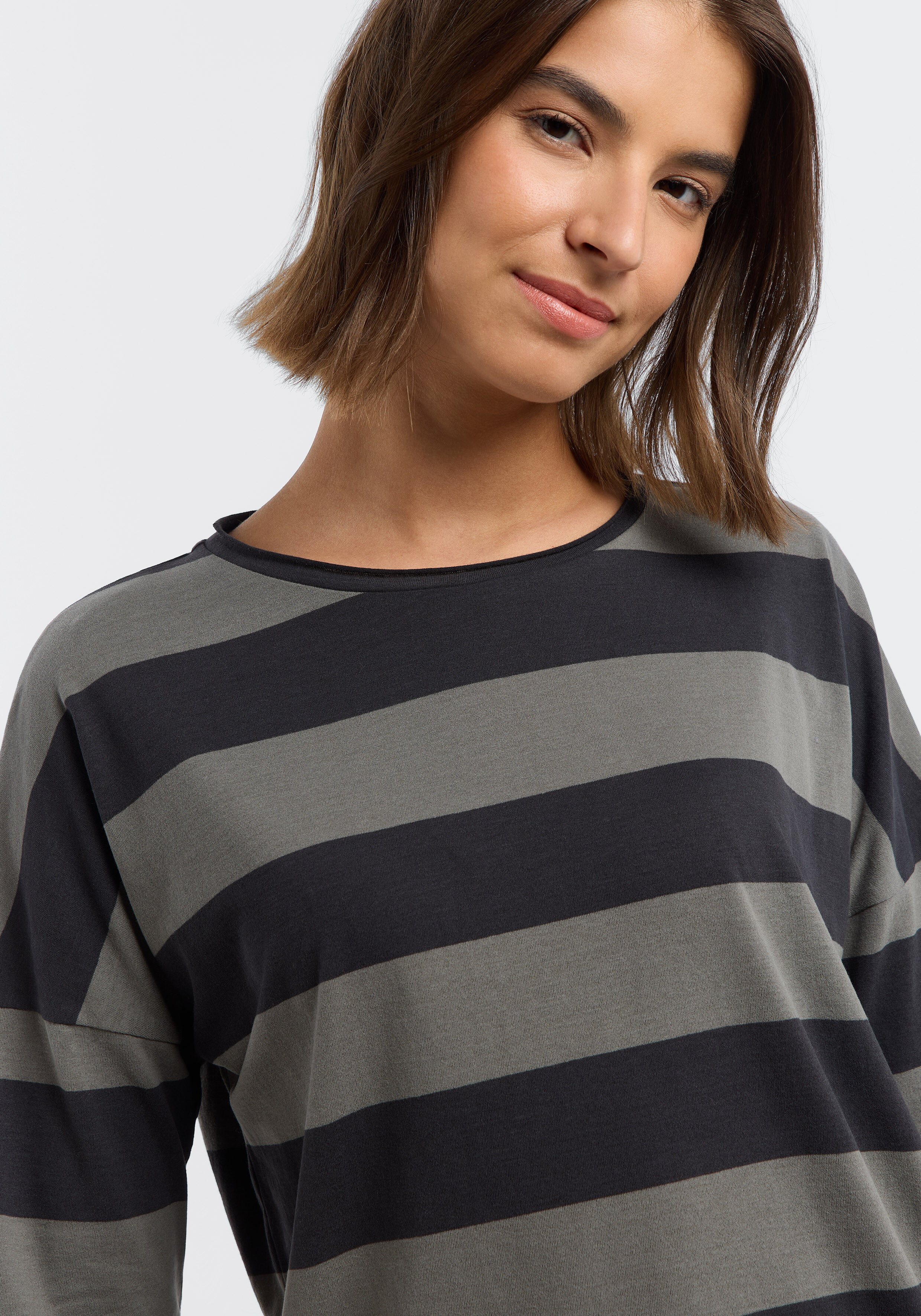 Frau trägt ein gemütliches, lässiges grau-schwarz gestreiftes Langarmshirt.