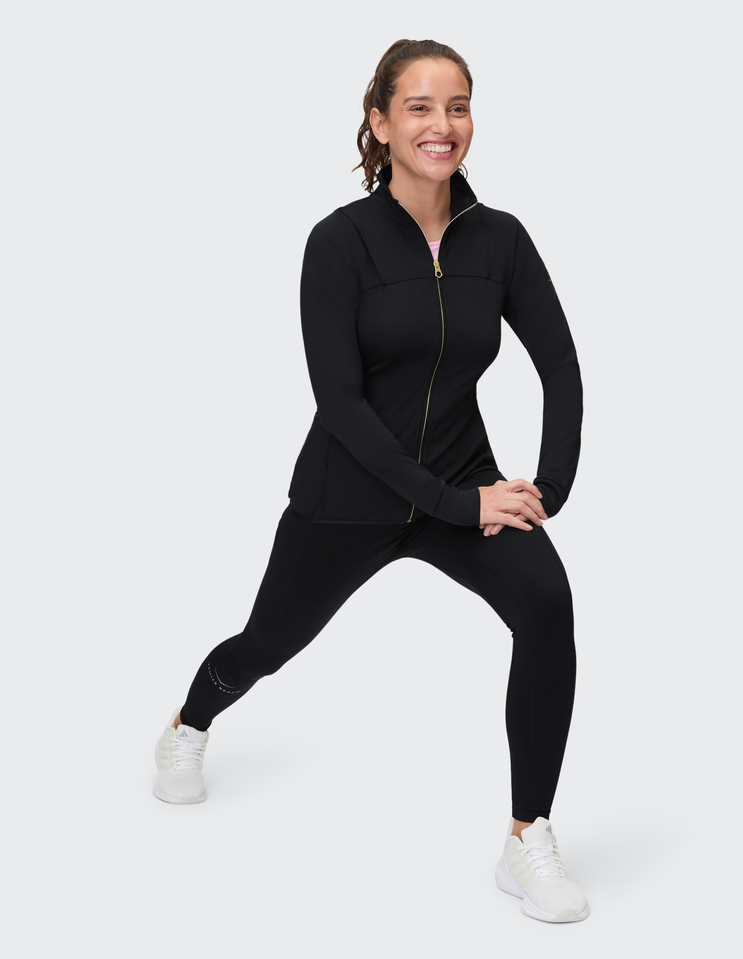 Frau in schwarzer Jacke mit Reißverschluss und Leggings, lächelnd in lässiger Pose.