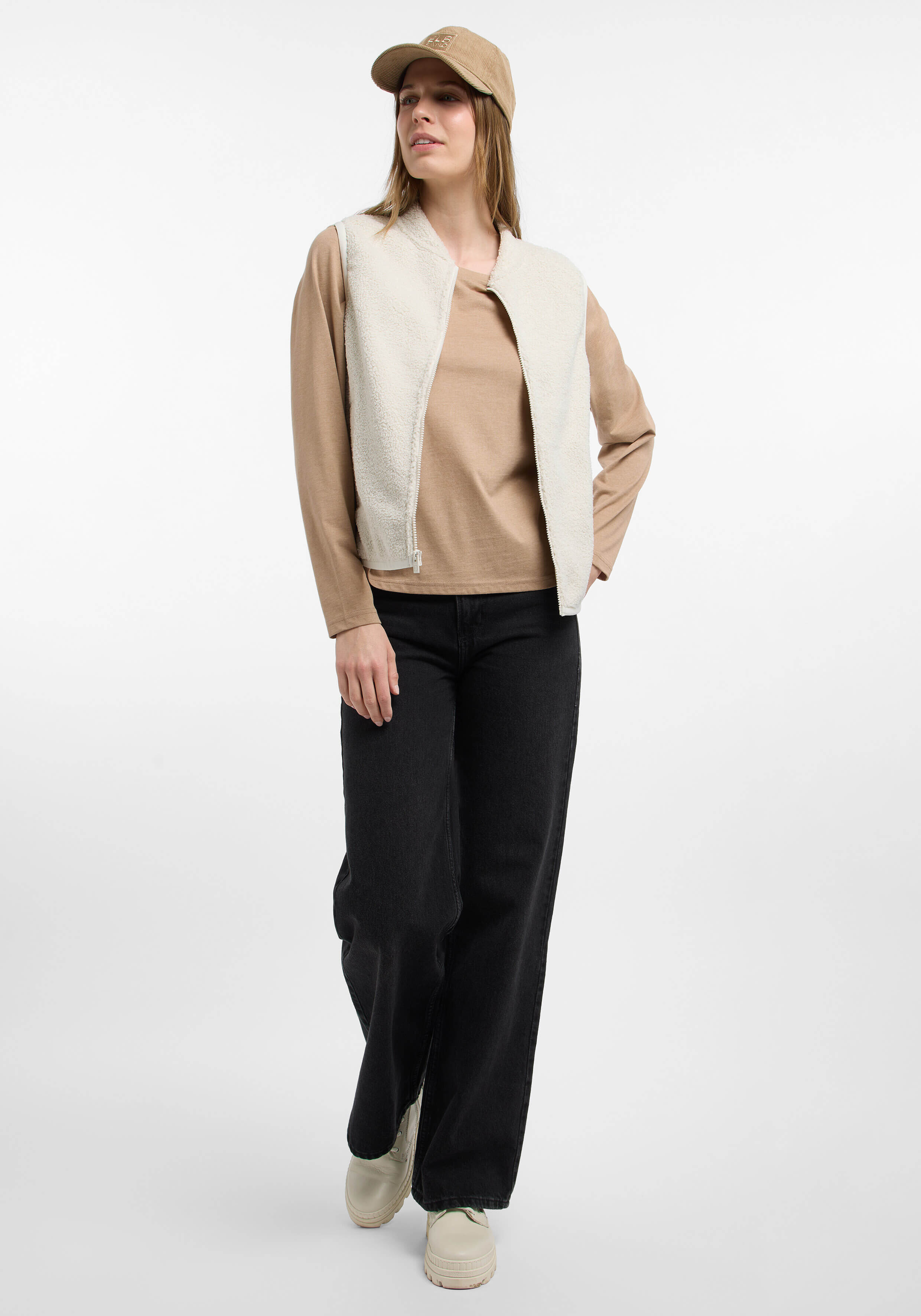 Frau trägt eine cremefarbene Fleeceweste, ein beiges Langarmhemd und schwarze Jeans.
