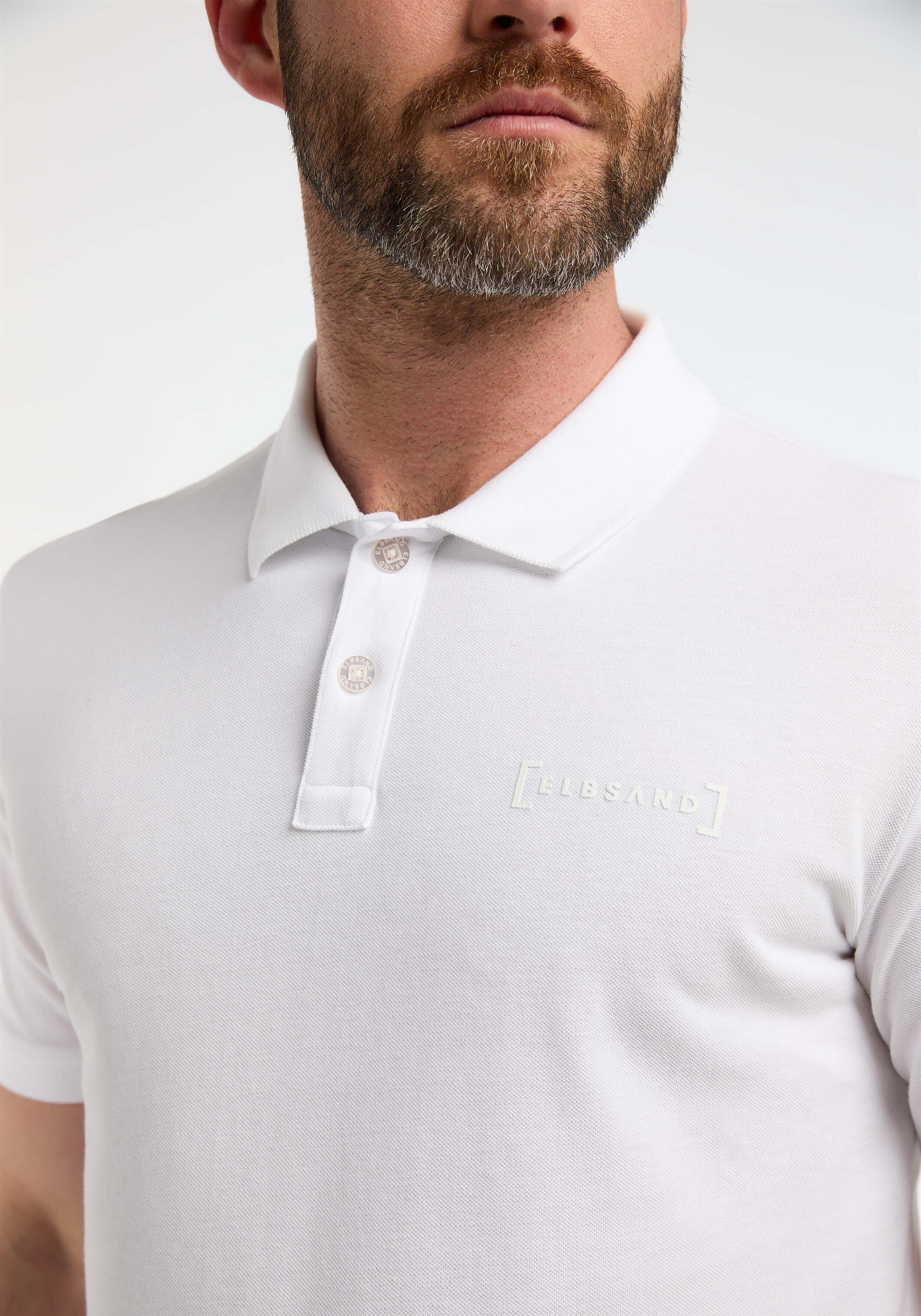 Nahaufnahme eines Mannes, der ein weißes Poloshirt mit ELBSAND-Logo trägt.